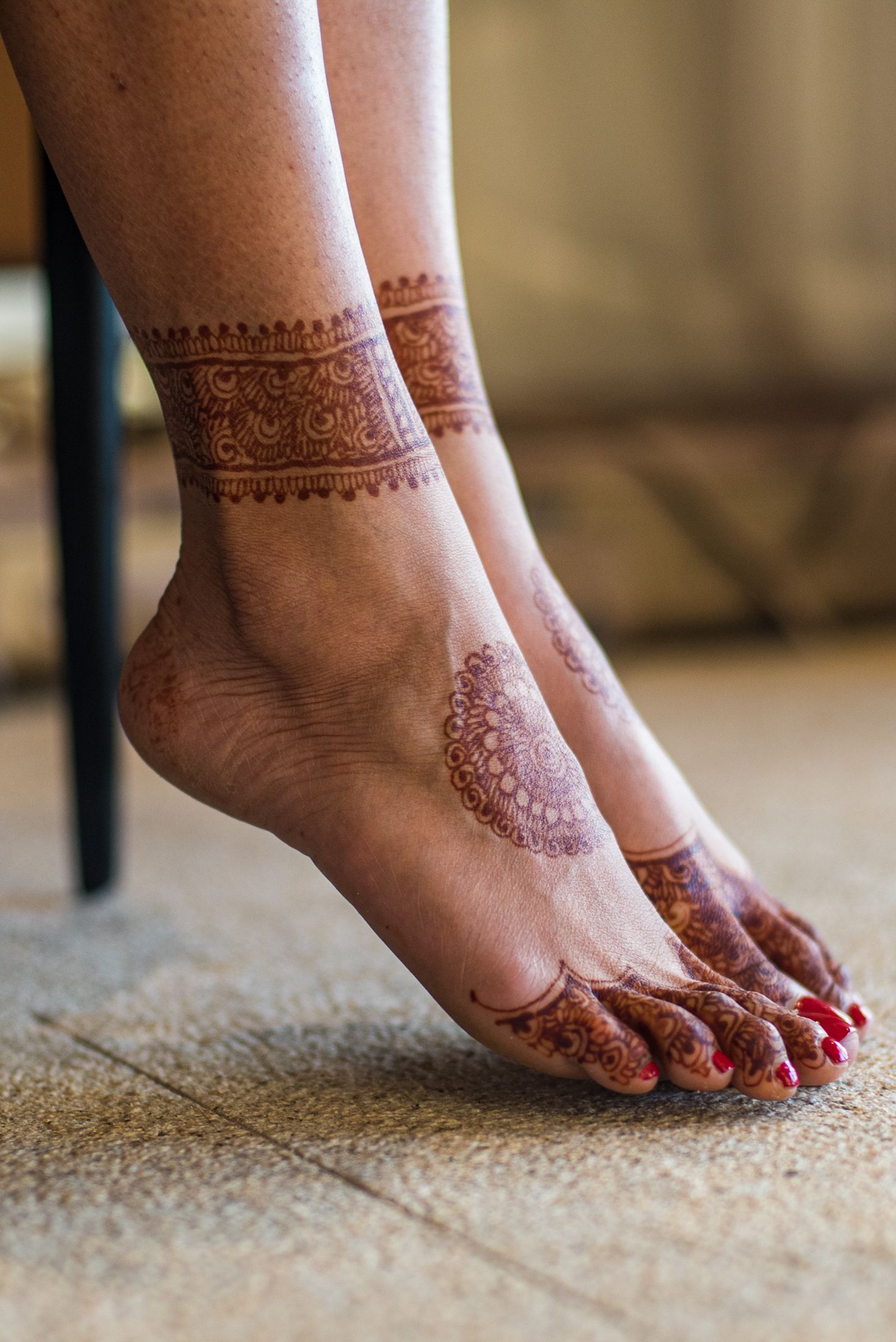 Intricate henna designs adorning feet with red nail polish against carpet.