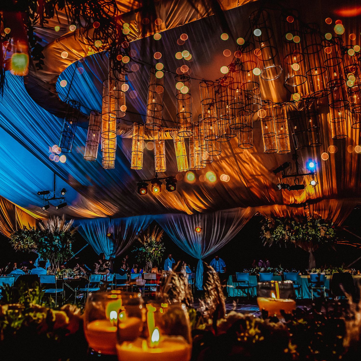 Dramatic tent reception with warm amber lighting and suspended floral installations creating an intimate atmosphere.