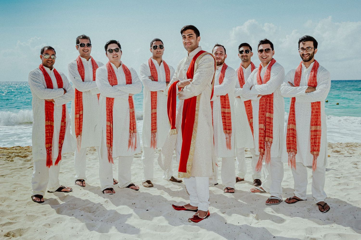Wedding party in red and white attire posing together on a tropical beach.