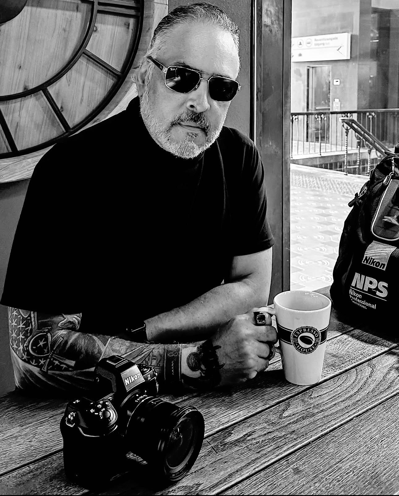 Black and white photos of camera equipment on wooden table in casual setting.
