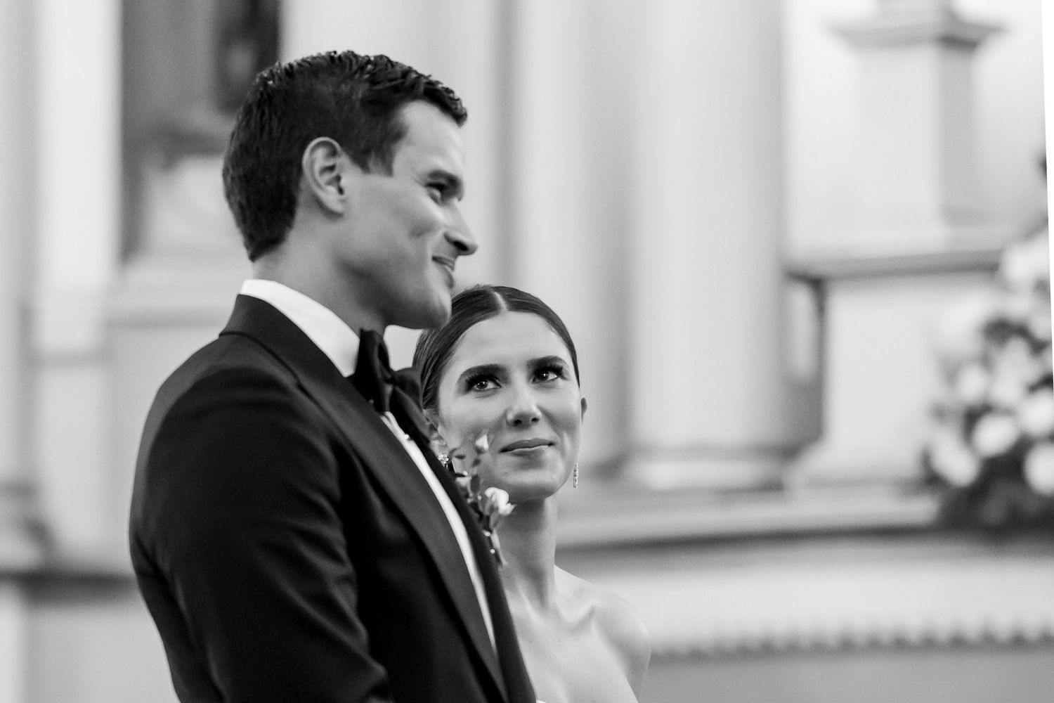 Black and white wedding photo of bride and groom standing at altar, looking forward with joy.