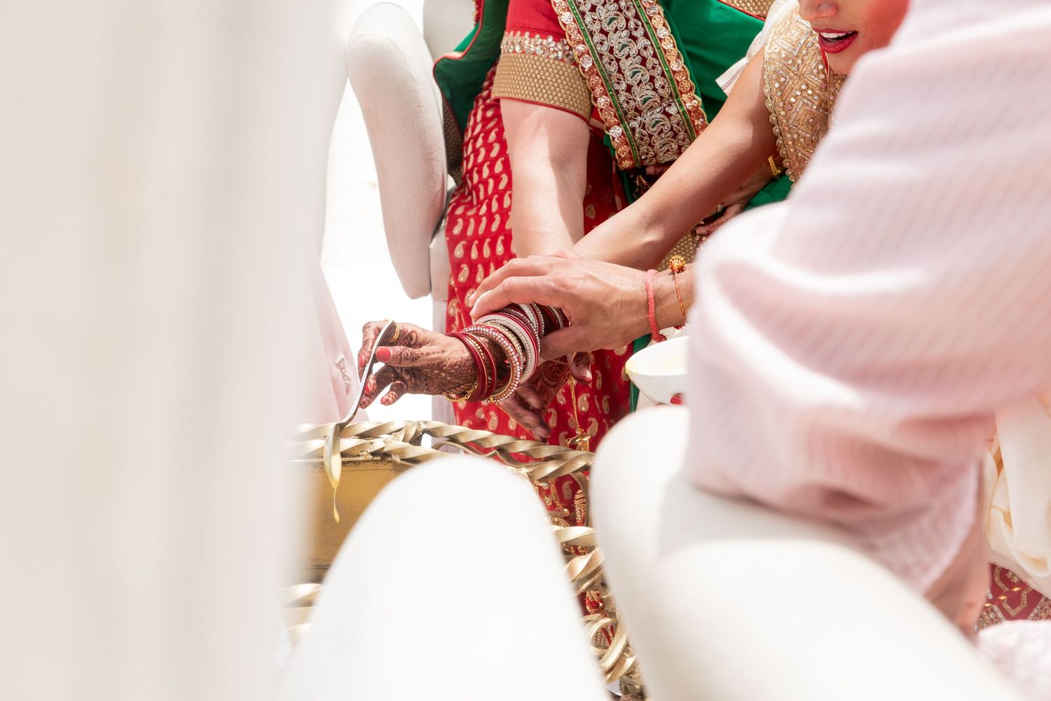 Close-up of hands adorned with mehndi during a traditional Indian wedding ceremony with colorful attire.