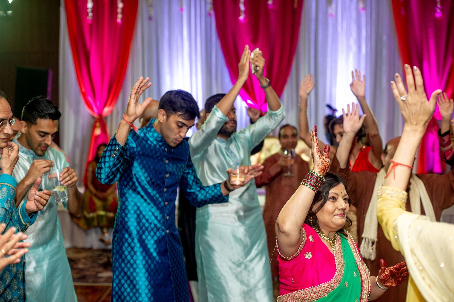 Guests dancing joyfully at a vibrant Indian wedding celebration with colorful traditional attire and festive decorations.