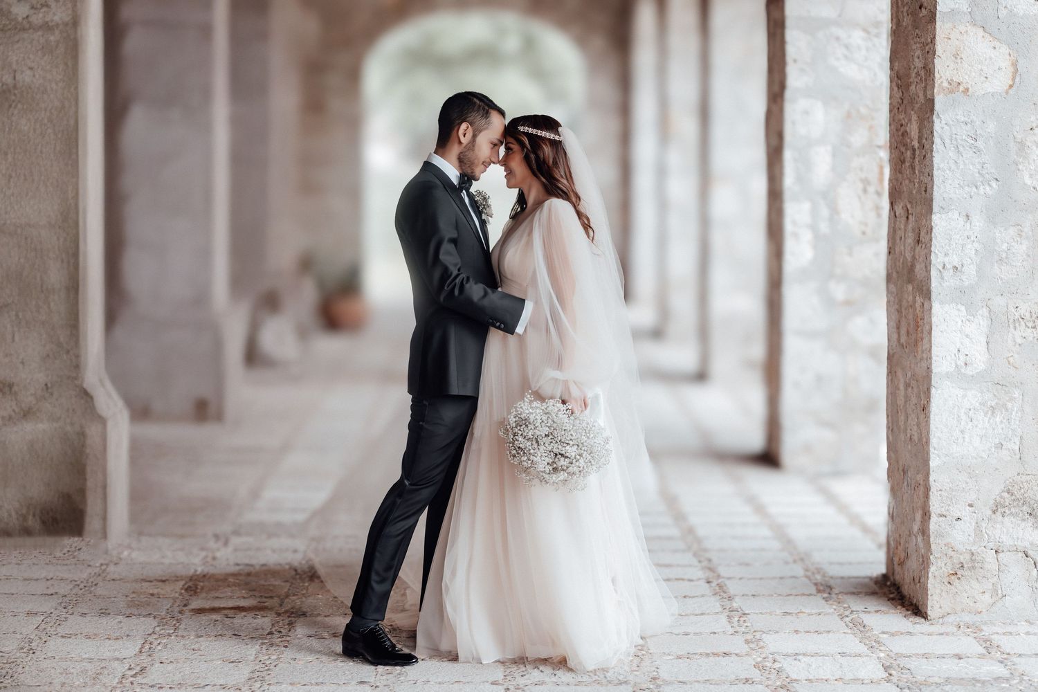 Bride and groom share romantic moments in a beautiful stone colonnade hallway.