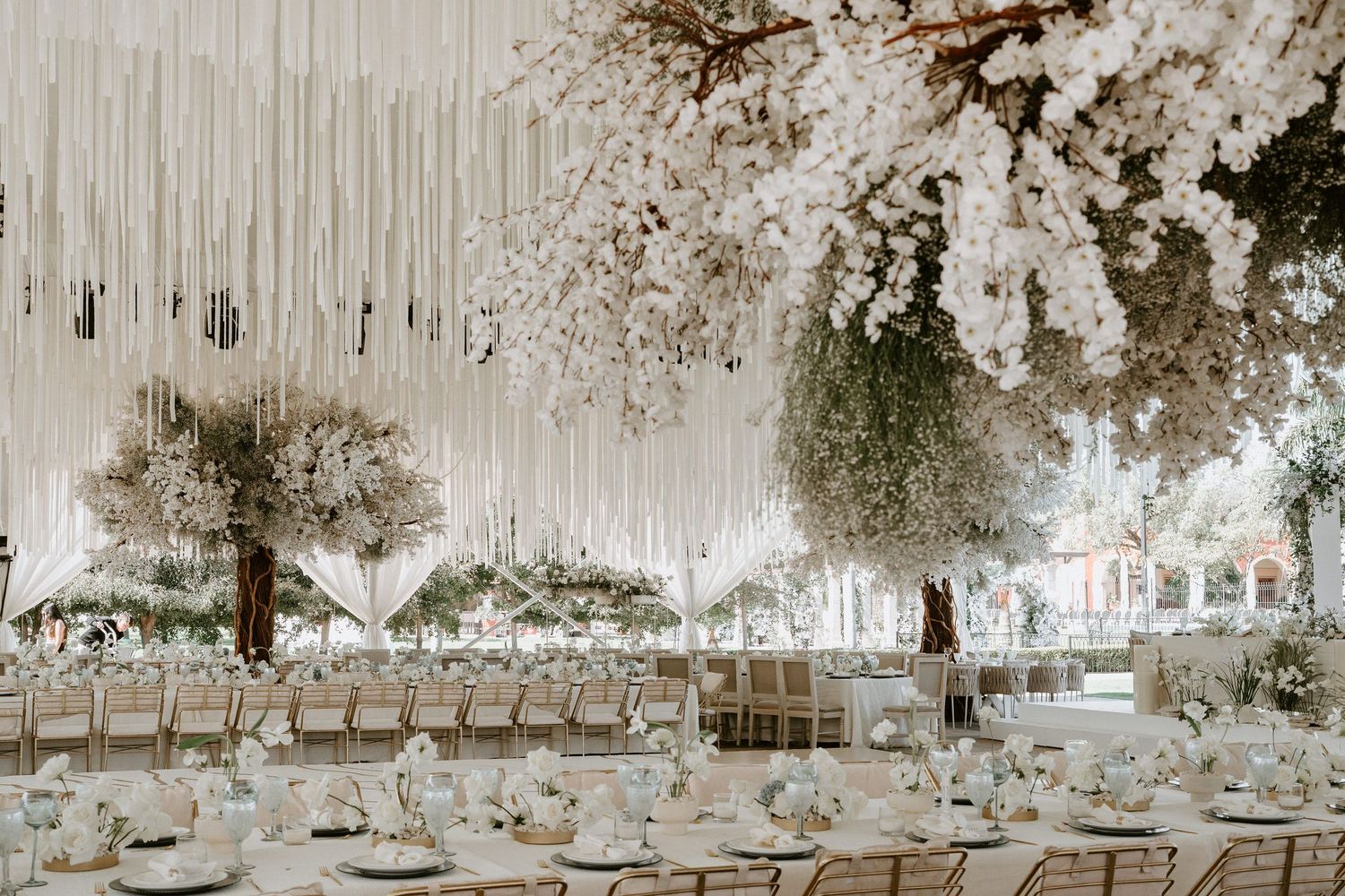 Panoramic view of a white-draped wedding venue with elegant table settings and suspended floral decorations.