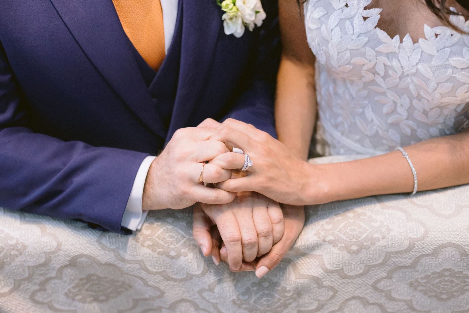 Close-up details of hands with wedding rings and formal attire.