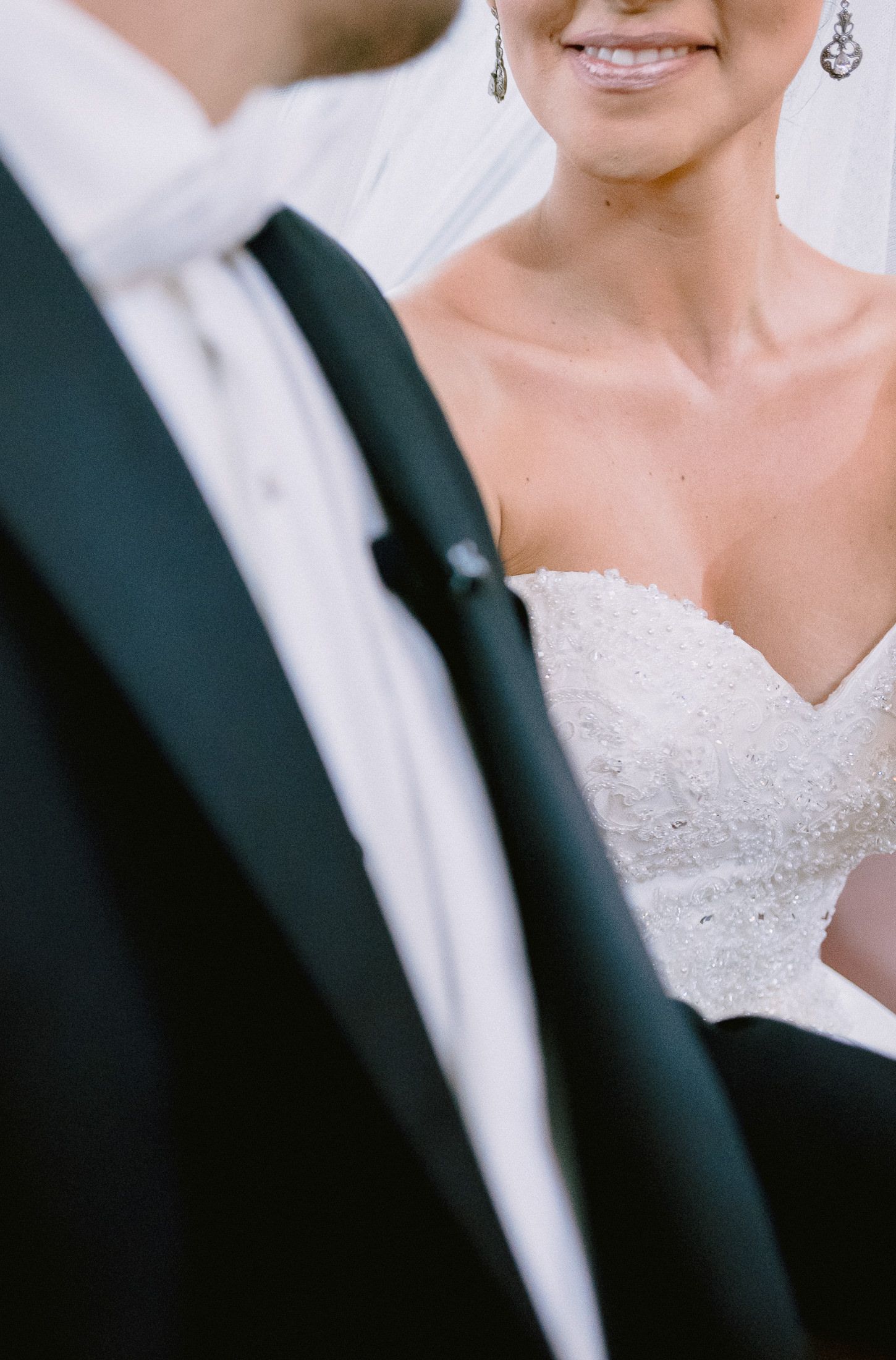 Detail shot of elegant white wedding dress next to black tuxedo.