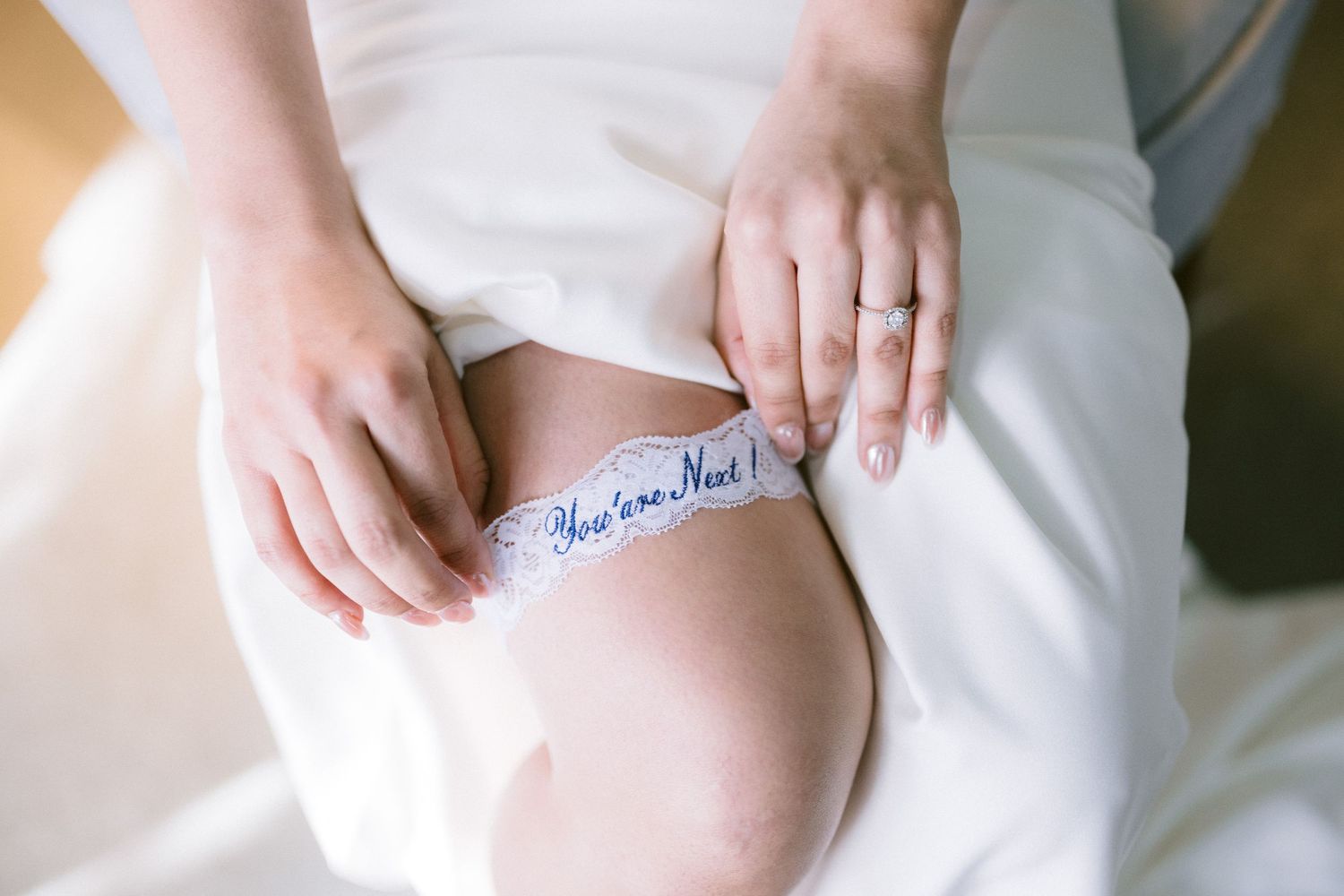 Wedding garter with blue text being adjusted on leg against white fabric.