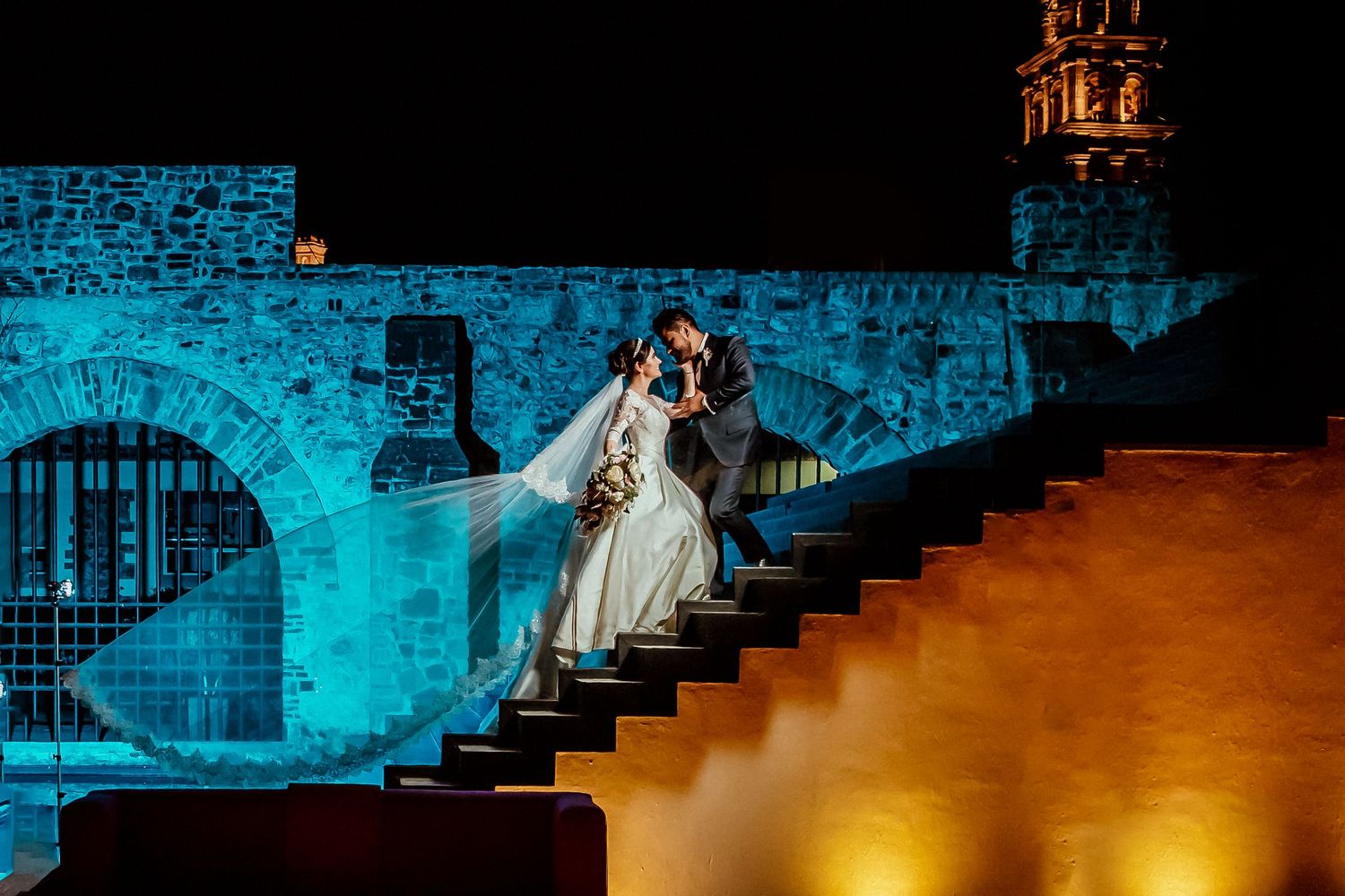 Dramatic nighttime wedding photography with blue lighting and stone architecture.