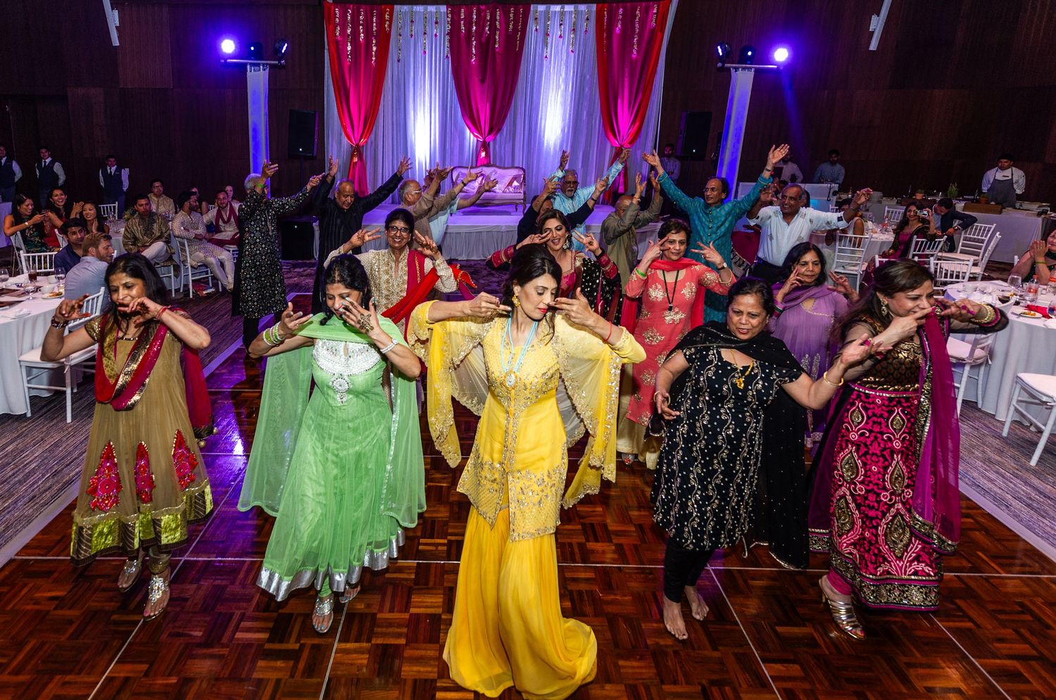 Women in colorful traditional Indian attire performing a choreographed dance at an elegant wedding reception.