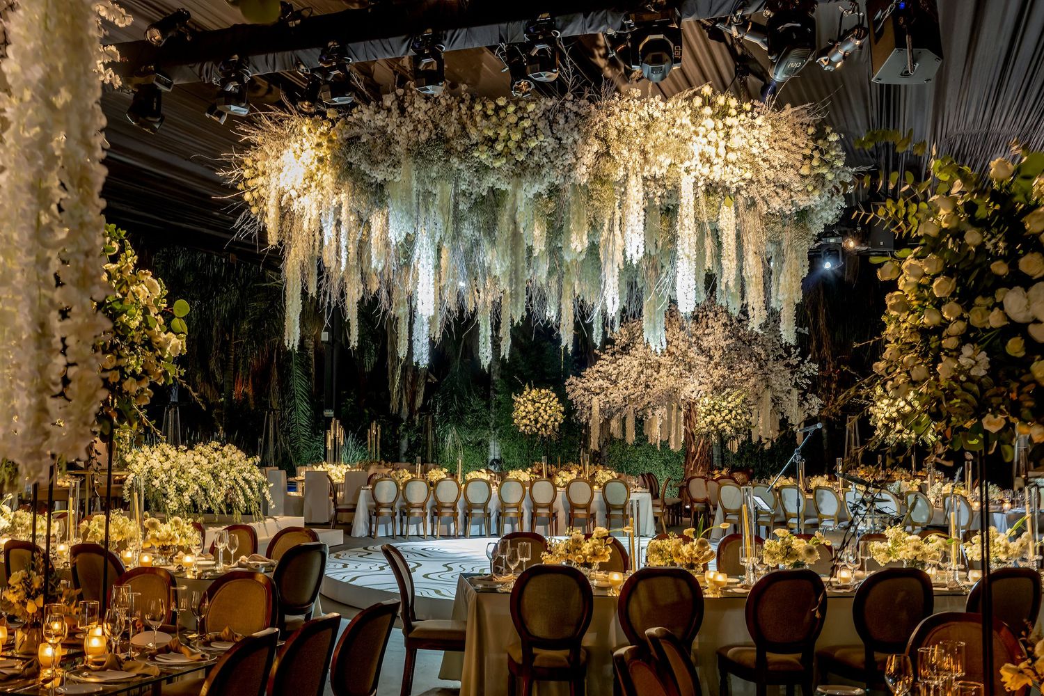 Luxurious wedding reception setup with hanging white drapes and warm lighting creating an ethereal ambiance.