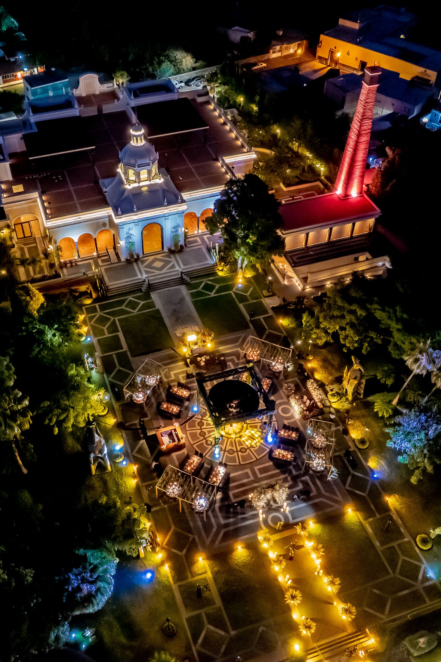 Aerial view of an illuminated outdoor venue with glowing pathways and architectural lighting at night.