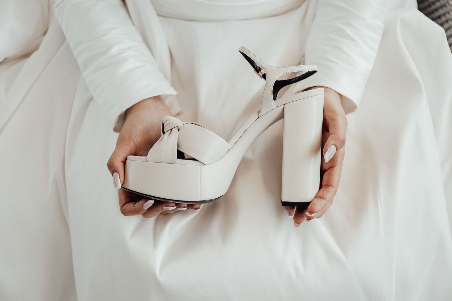 White platform wedding heels held against white fabric background.