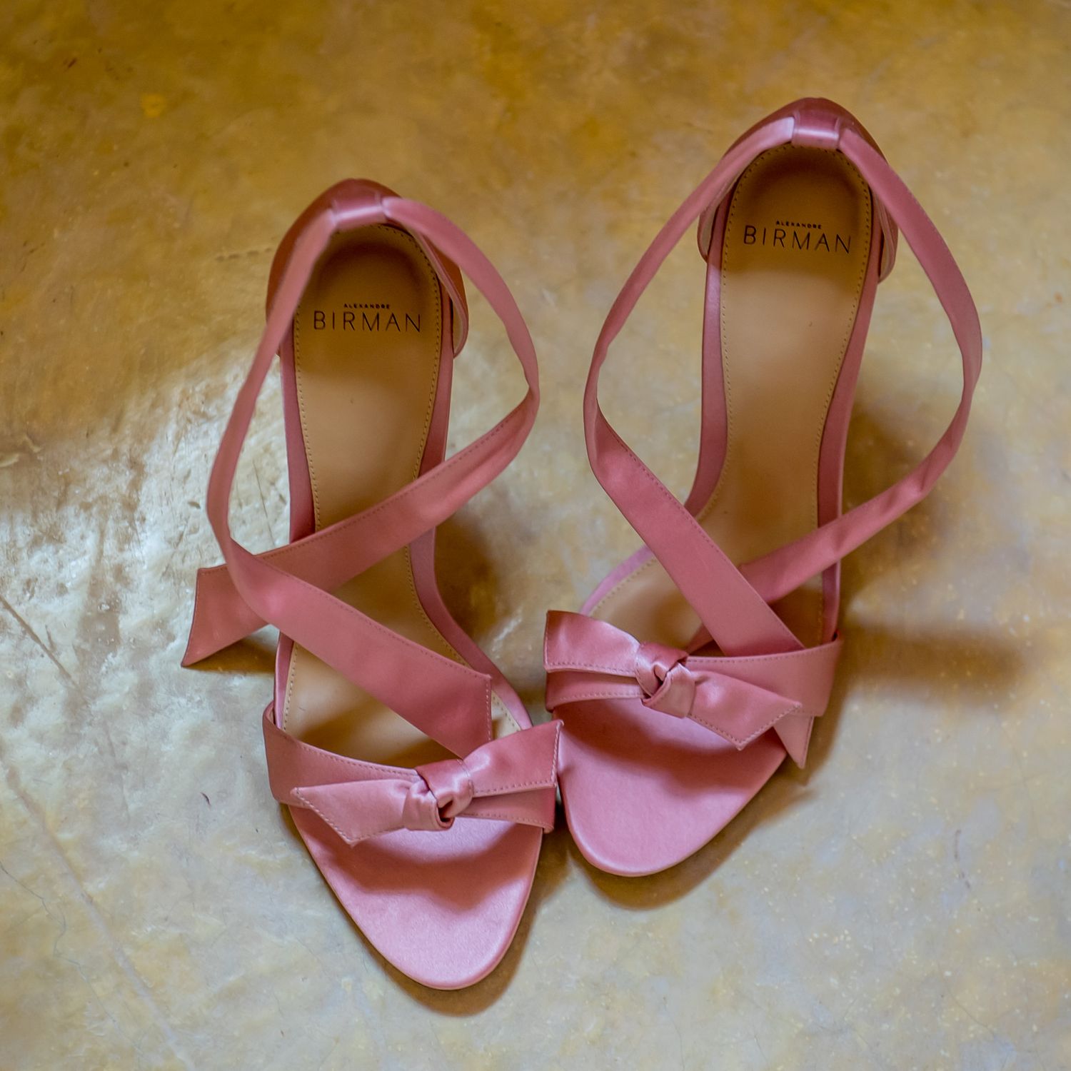 Pink leather bridal sandals photographed against a textured golden background.