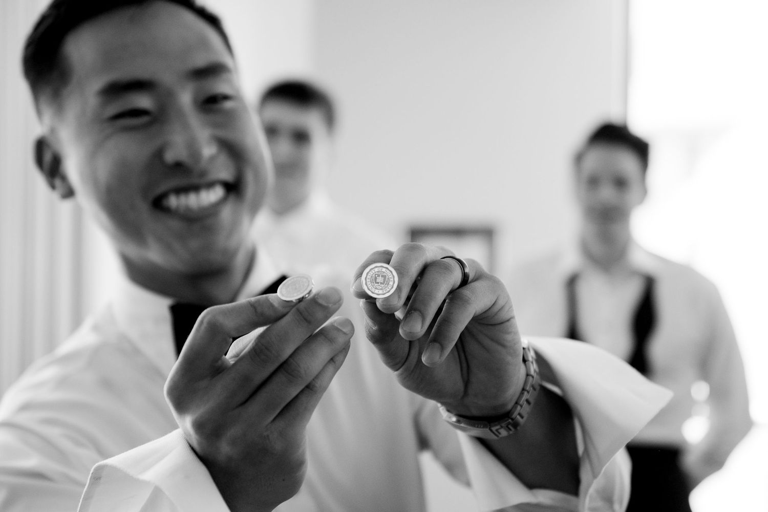 Smiling groom holding up a watch in black and white photo with groomsmen in background.