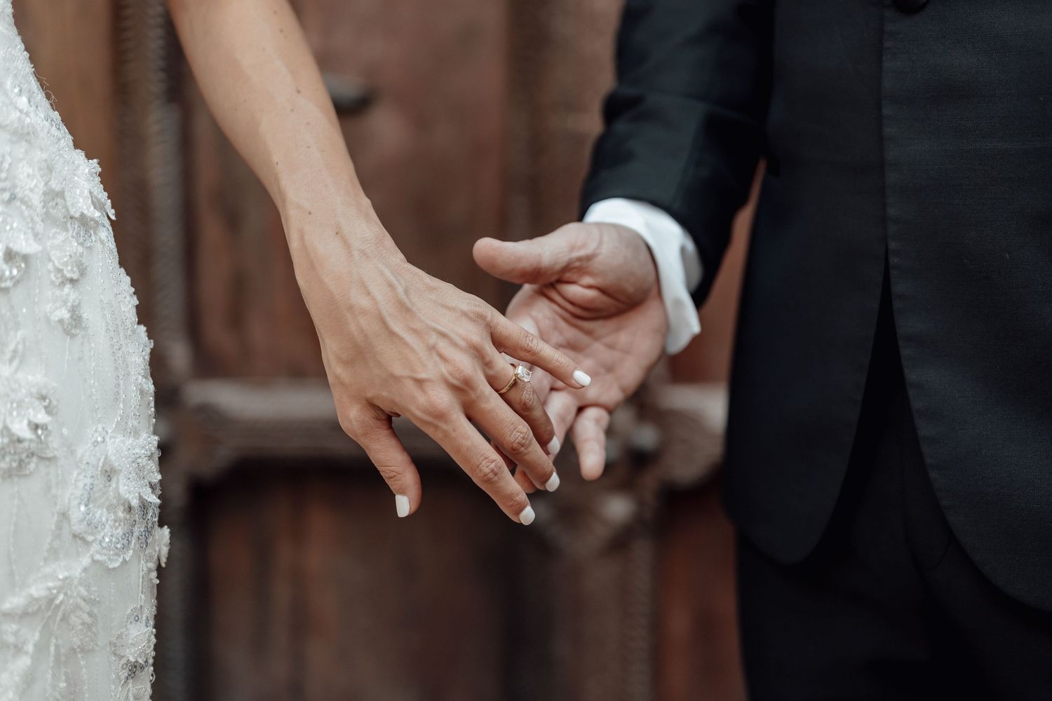 Bride and groom holding hands showing wedding rings, close-up shot of couple in wedding attire.