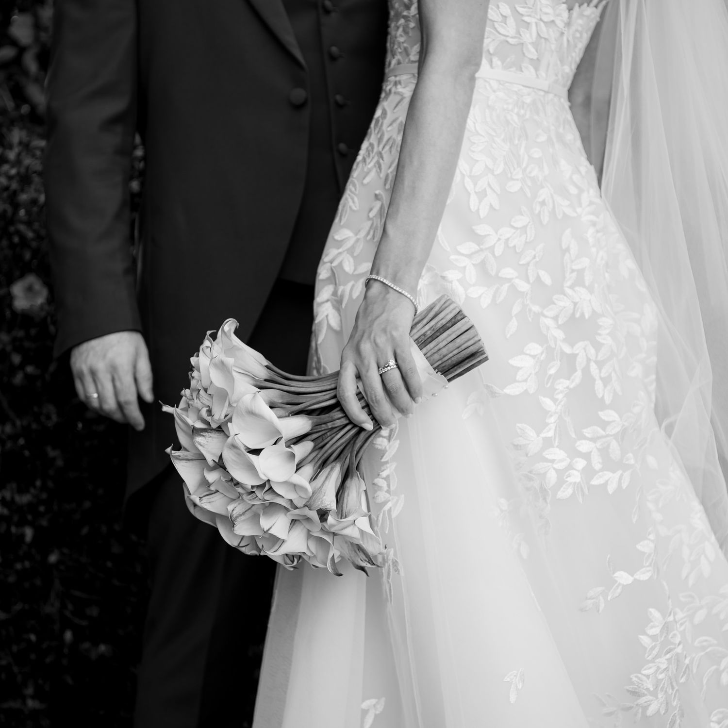 Black and white detail shot of wedding attire and floral bouquet arrangements.