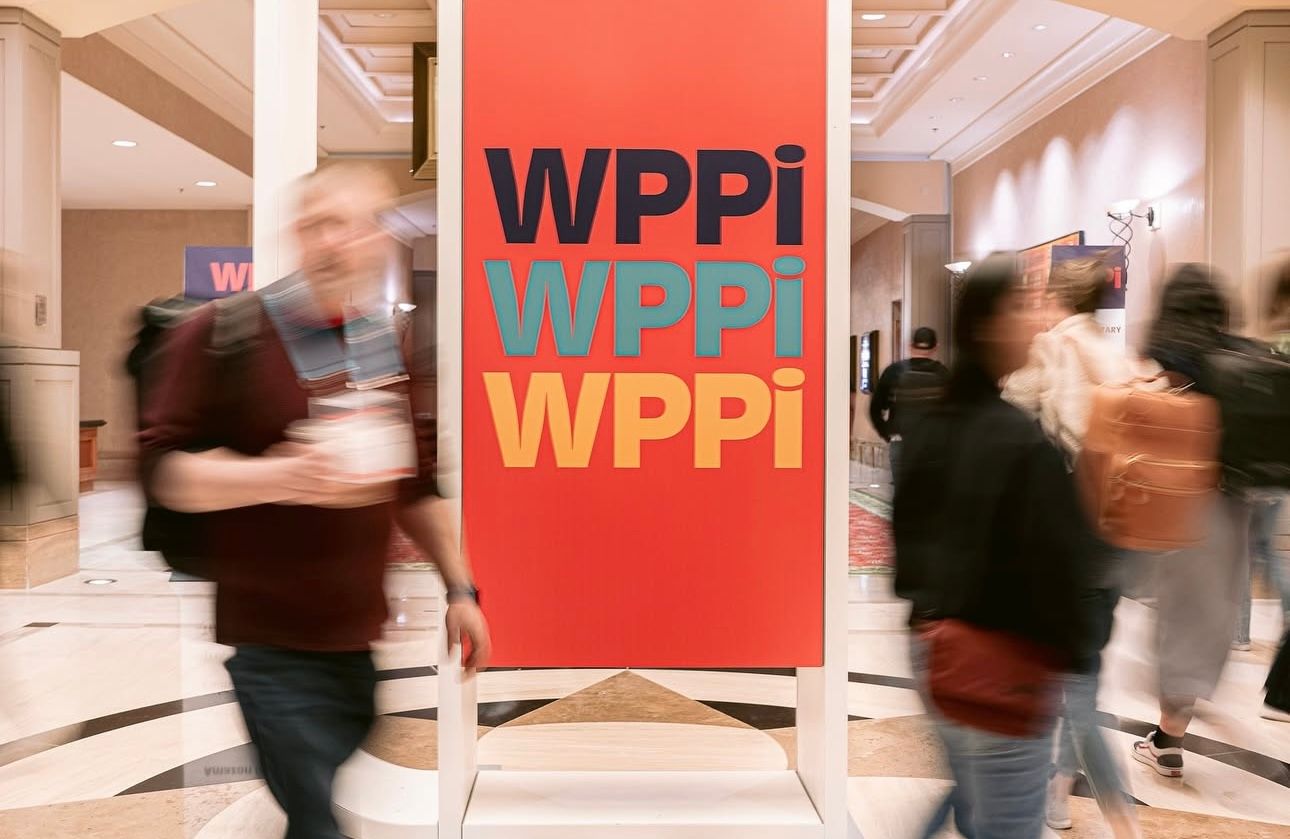 Motion-blurred hallway with red WPPi branding showing people walking through the space.