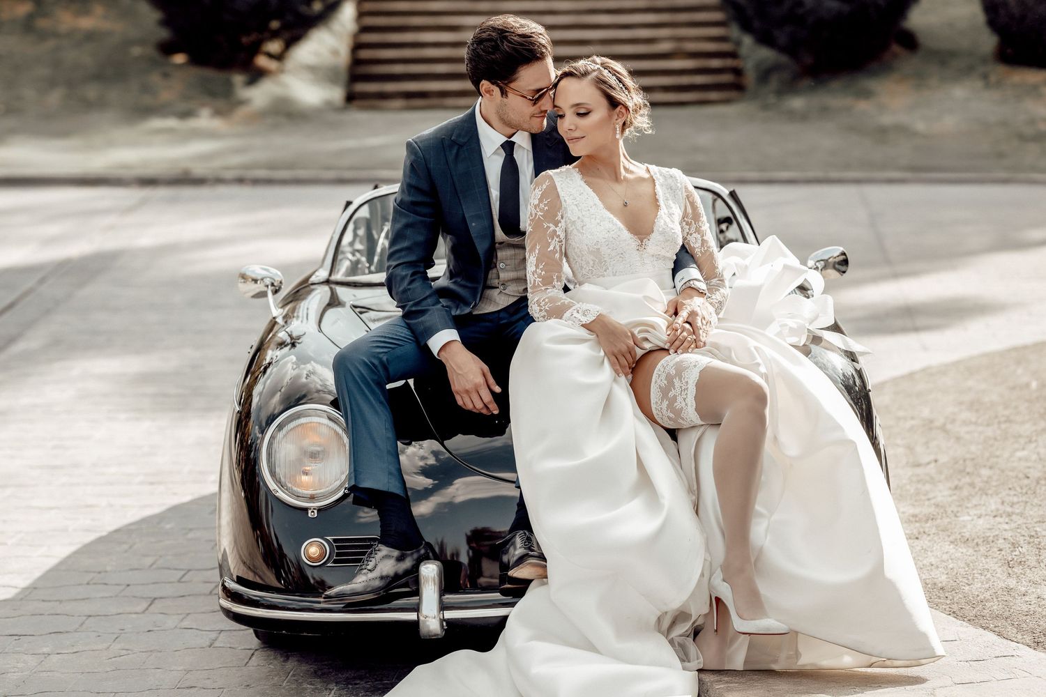 A romantic wedding couple poses with a vintage Volkswagen Beetle car in an outdoor setting.