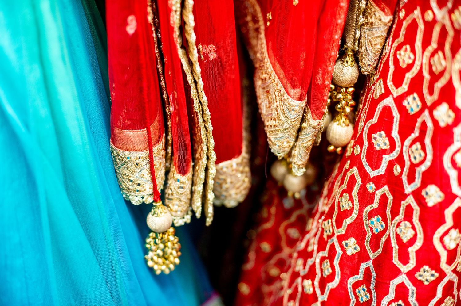 Vibrant Indian bridal lehengas in red and turquoise with gold embroidery and pearl tassels hanging on display.