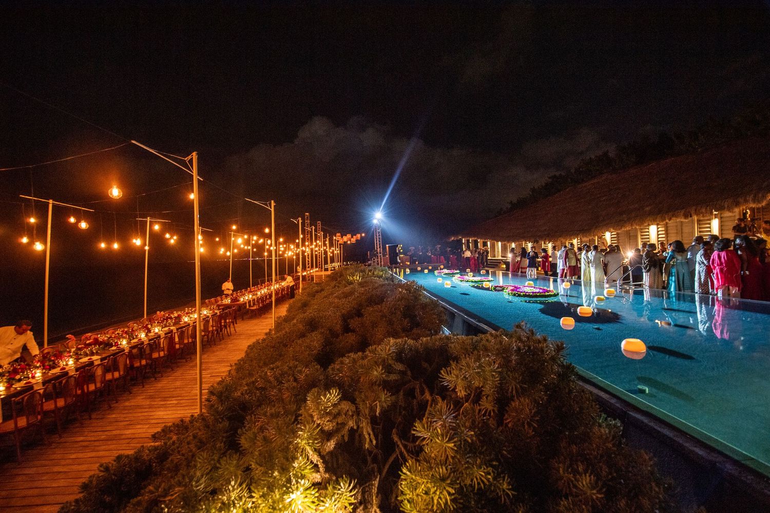 Outdoor beachside dining event at night with string lights, pool, and guests along a cliffside terrace.