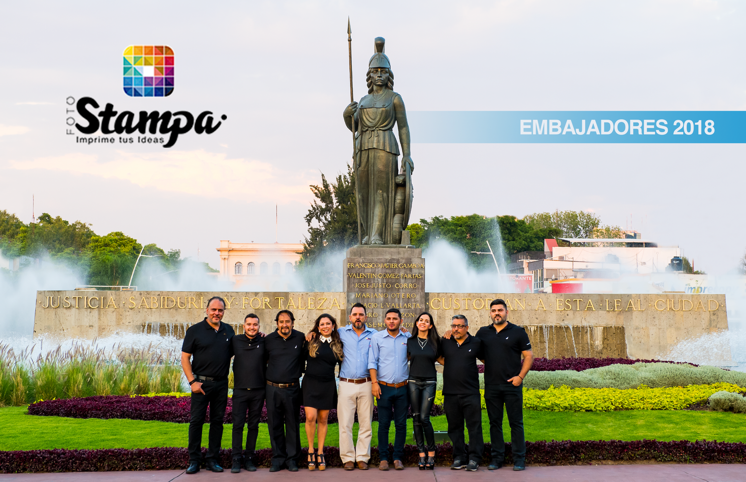 Group photo of business ambassadors standing in front of a large statue and fountain at sunset.