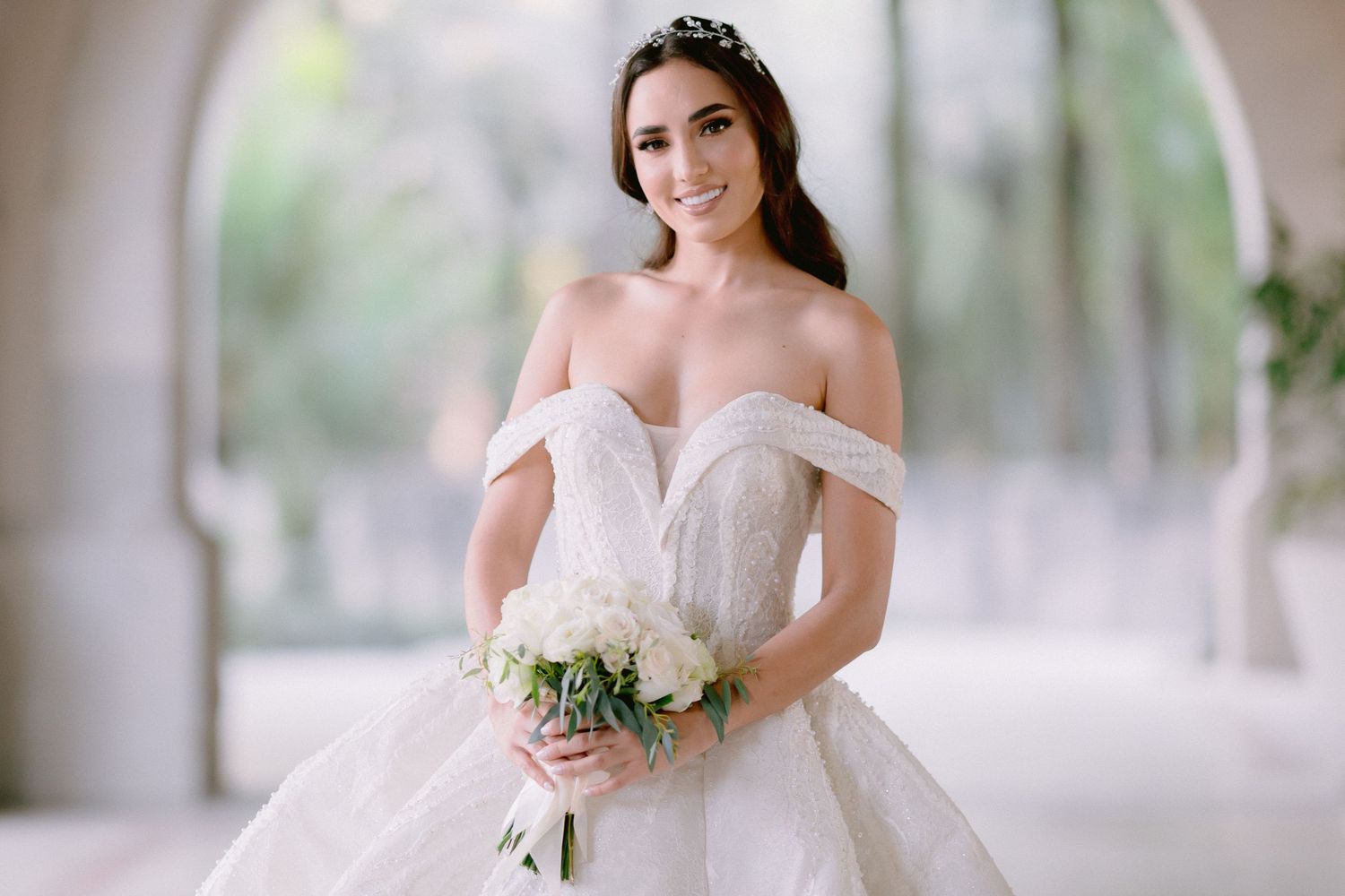 Romantic bridal portrait featuring off-shoulder gown and delicate floral crown in soft lighting.
