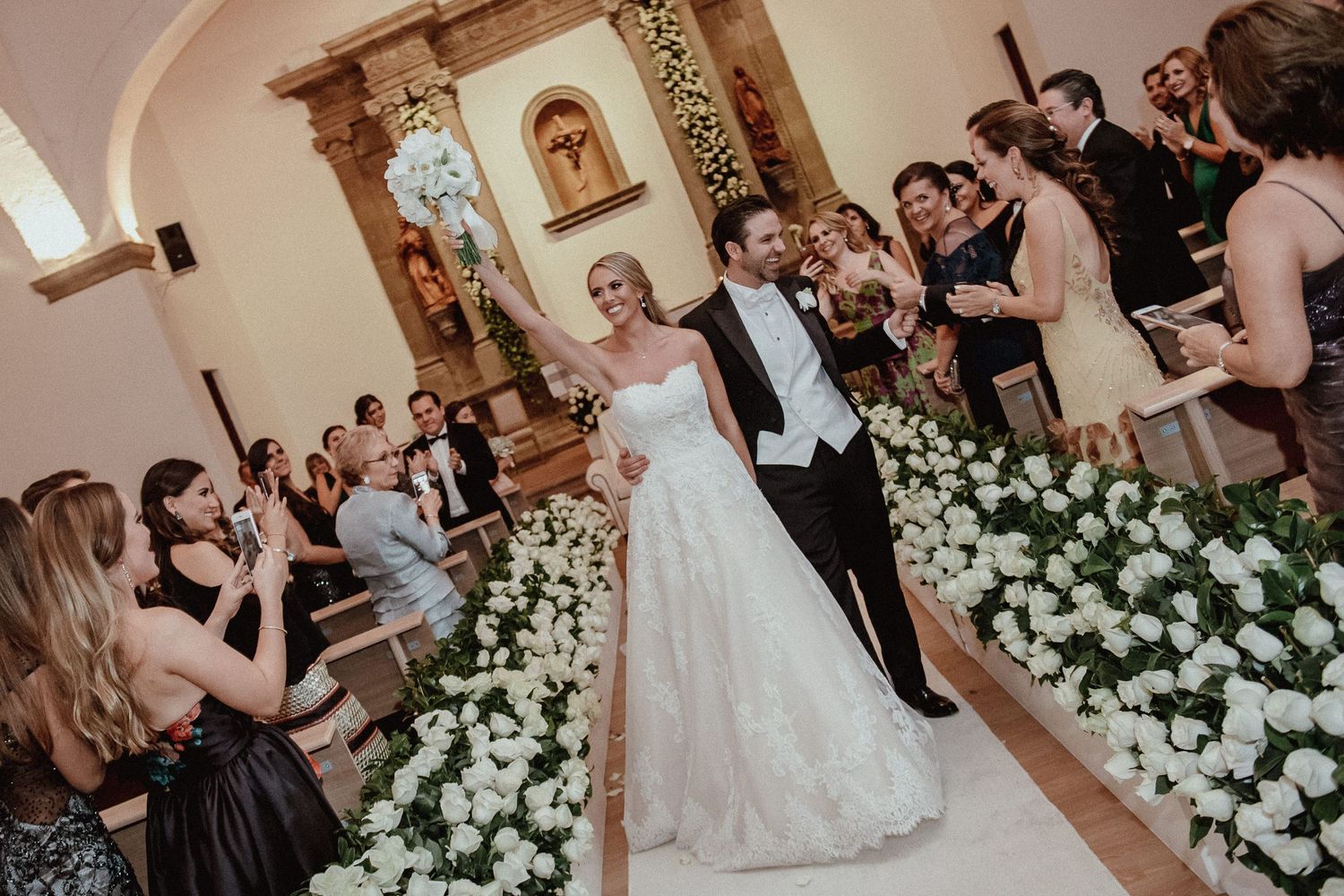 Indoor wedding reception with white floral decorations and dancing guests.