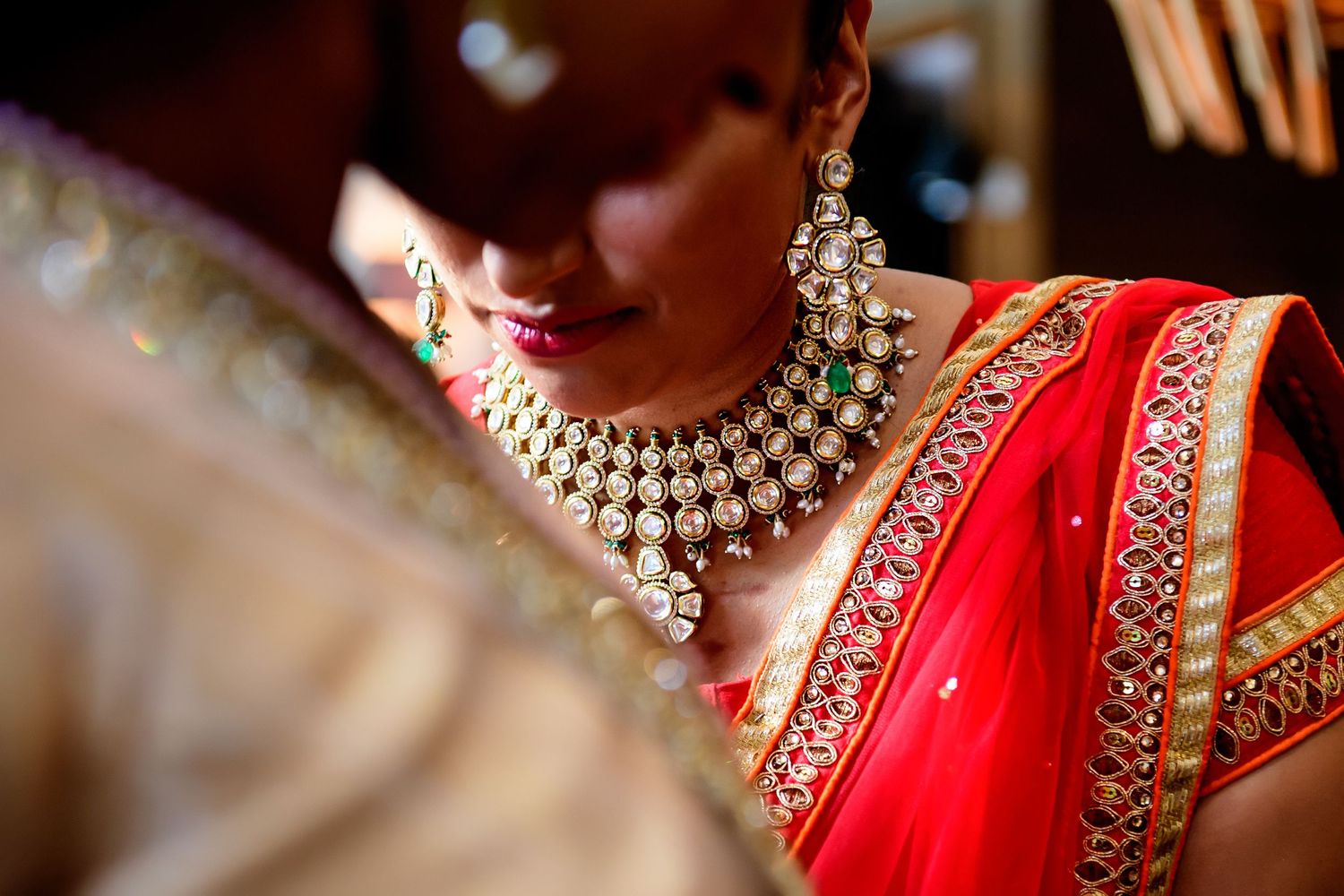 Indian bride in red saree wearing elegant kundan necklace and earrings at a traditional wedding ceremony.