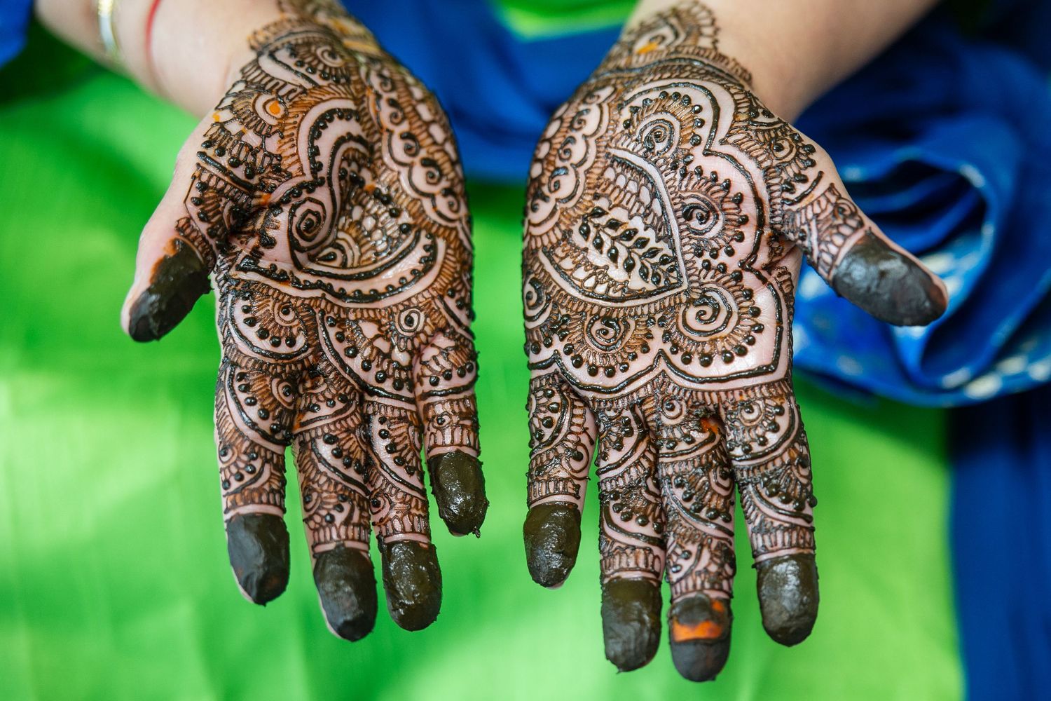 Intricate henna mehndi designs on both palms of a woman's hands with floral and paisley patterns.