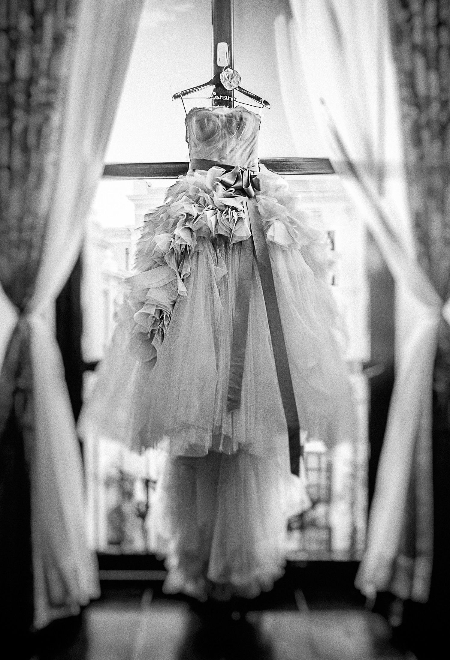 Wedding dress hanging in front of sunlit window creating a dreamy silhouette effect.