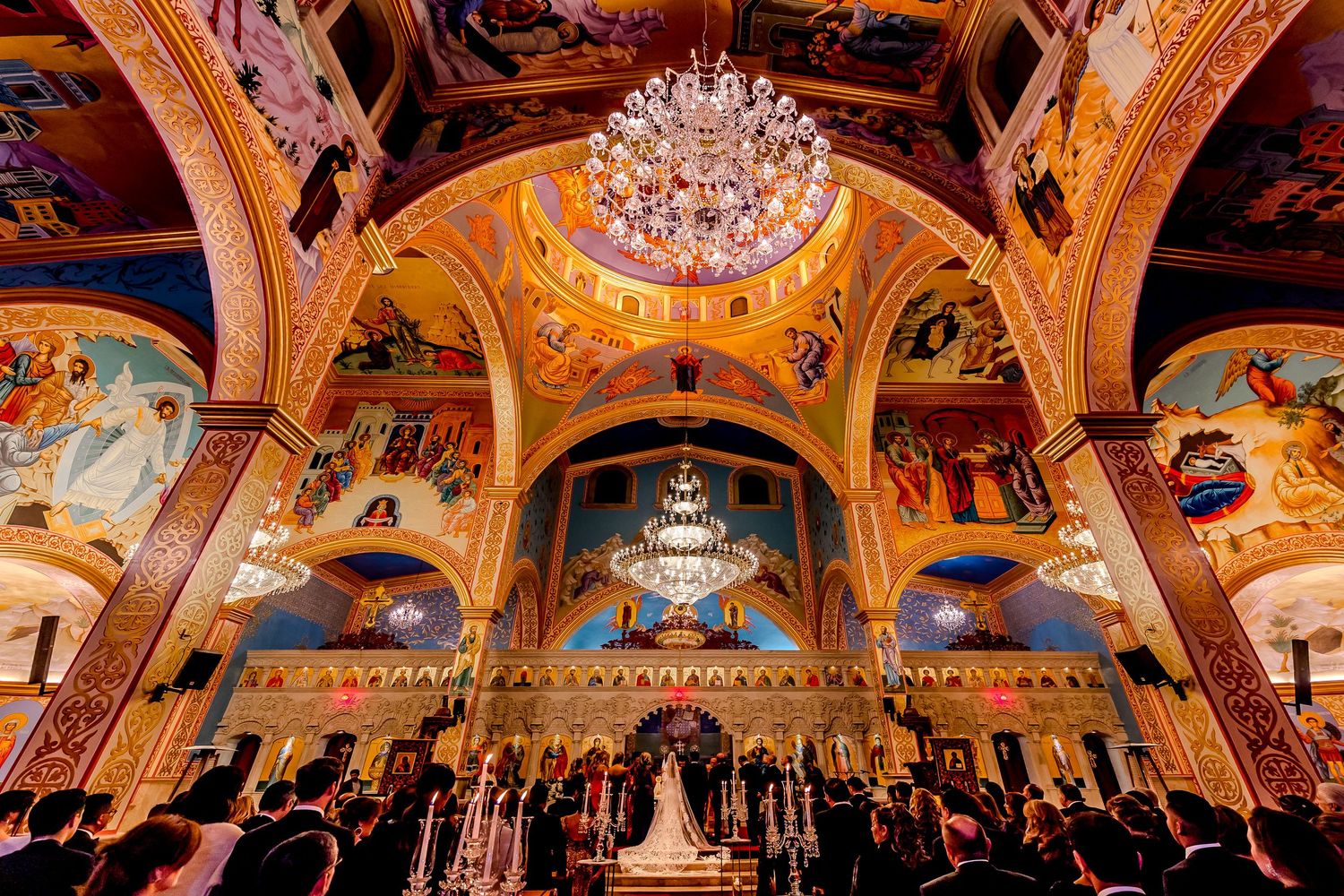Panoramic view of an ornate church interior with painted ceilings and crystal chandeliers.