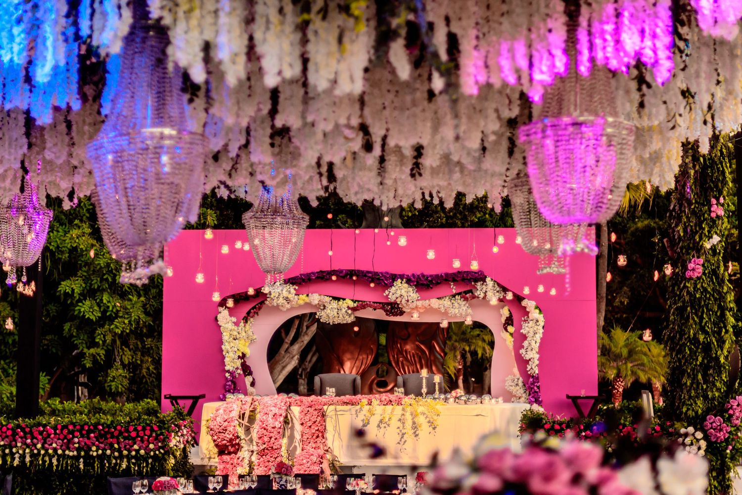 Wedding reception decor featuring dramatic pink and blue lighting with hanging floral arrangements.