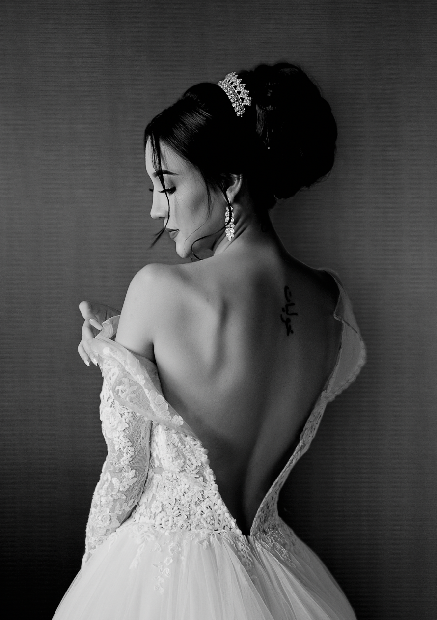 An artistic black and white bridal portrait showing the back detail of a lace wedding gown.