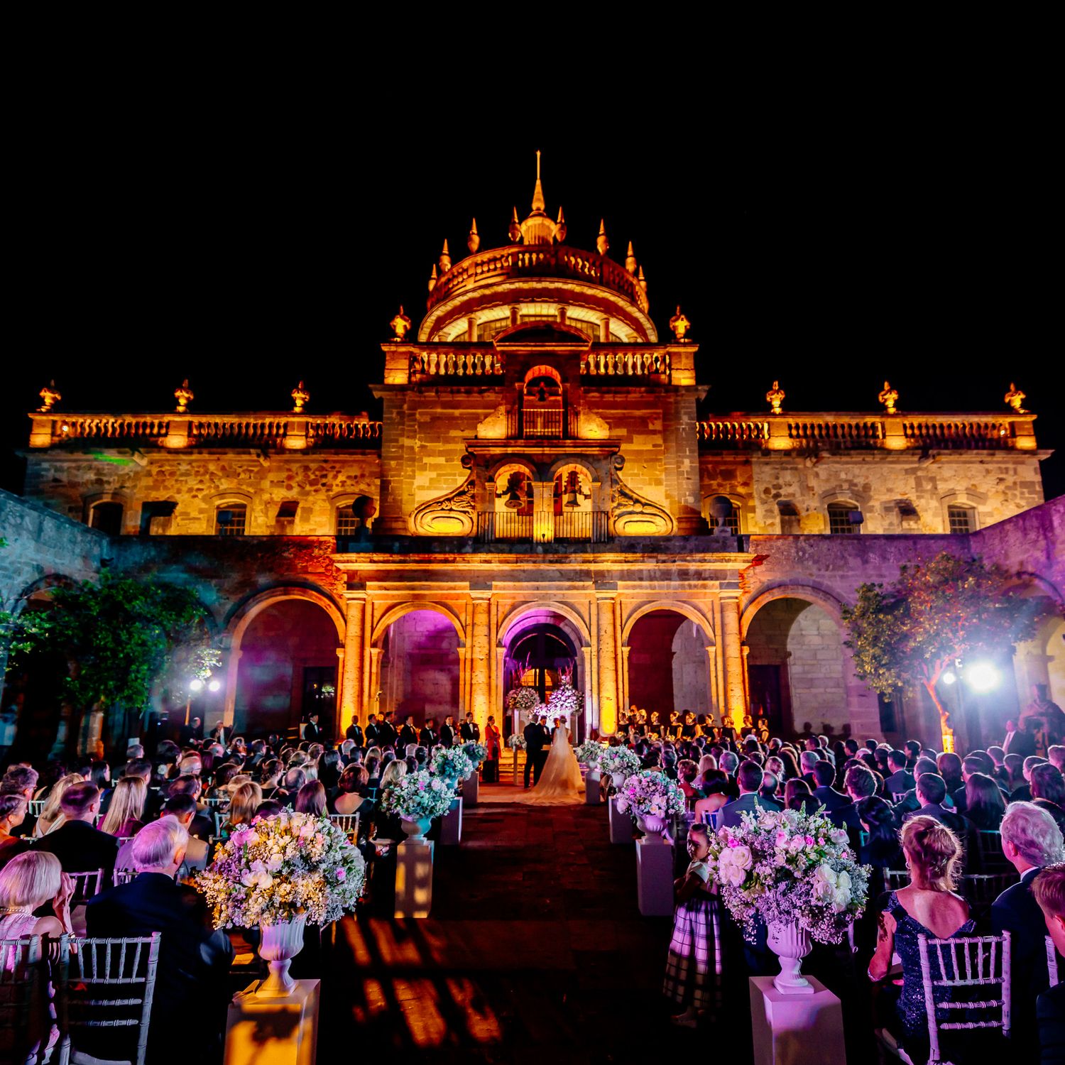 Historic palace illuminated at night with outdoor reception seating and colorful lighting.