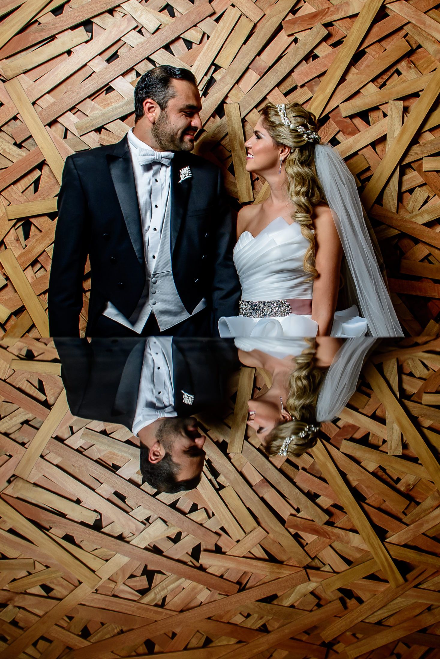 Elegant couple posing against wooden geometric wall pattern at wedding venue.