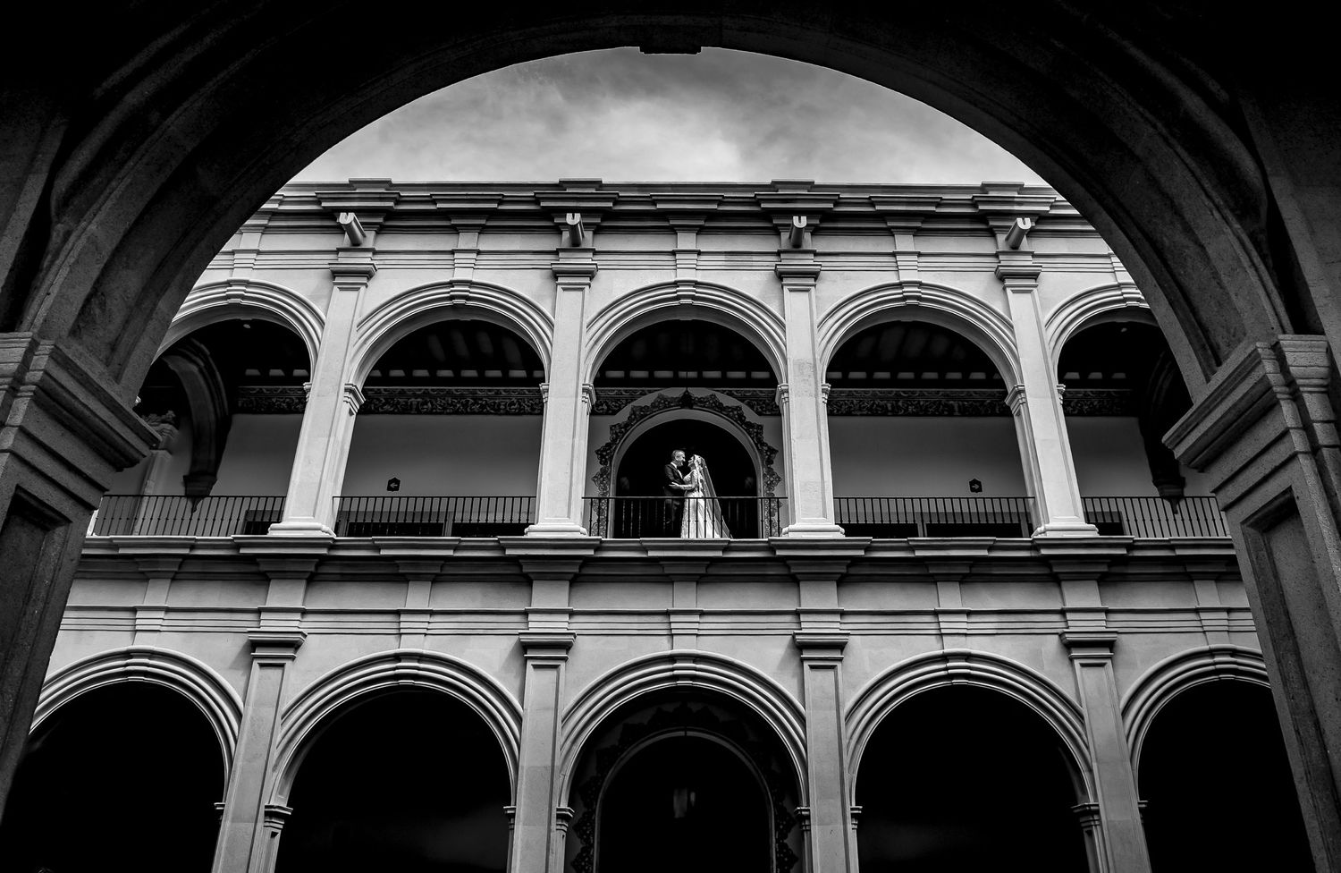Black and white architectural wedding photo featuring classical arches and columns.