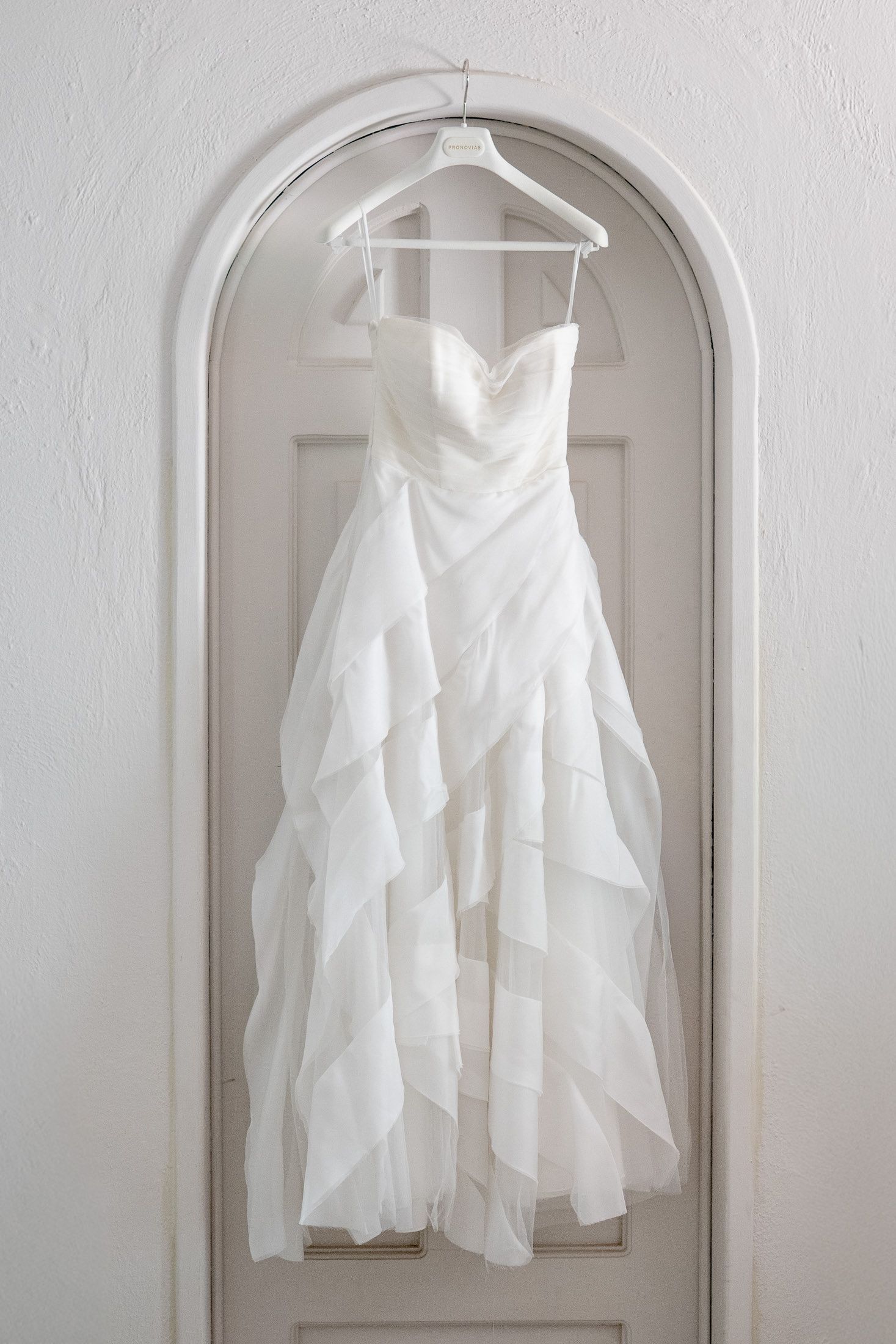 White wedding dress hanging in arched doorway against light wall.