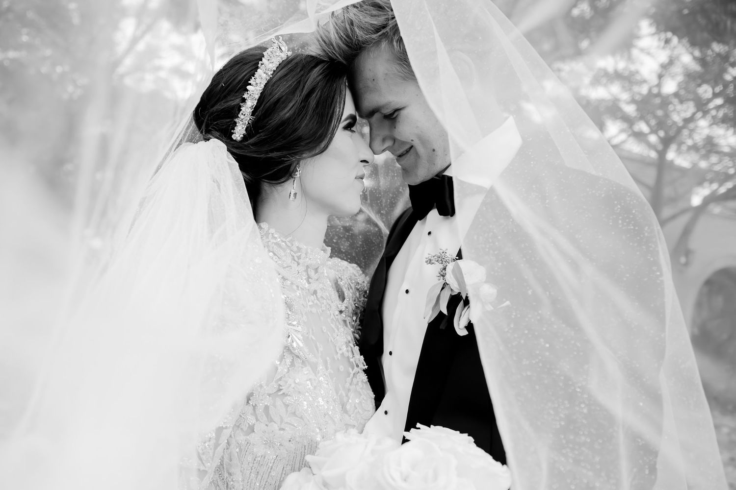 Black and white wedding photo of bride and groom sharing an intimate moment under a flowing veil.