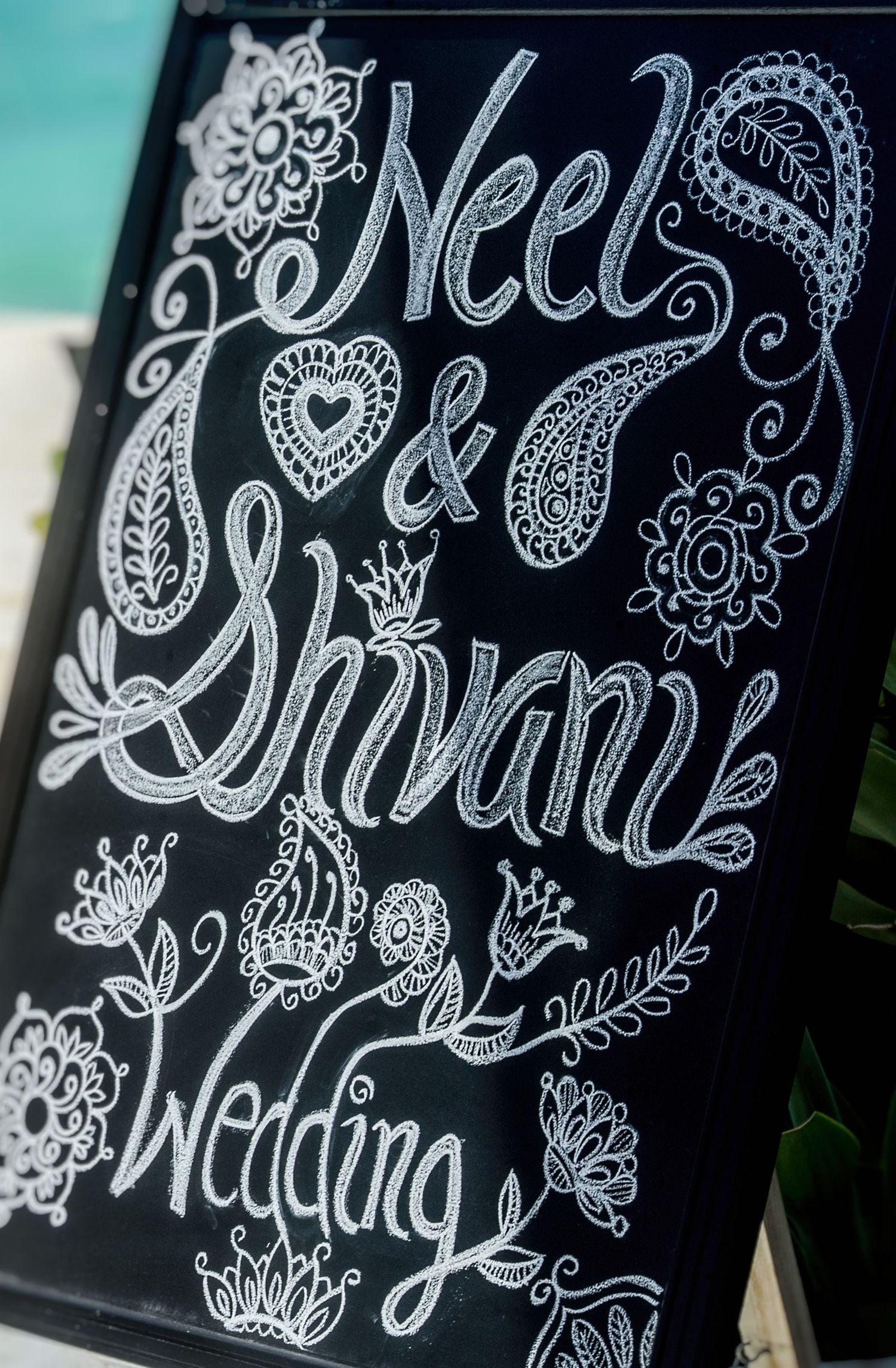 Elegant chalkboard wedding sign for Neel and Shivani featuring intricate white floral and paisley hand-lettered artwork.