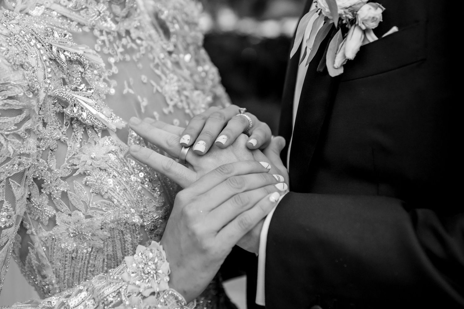 Black and white photo of a couple exchanging wedding rings during a ceremony, bride in lace gown.