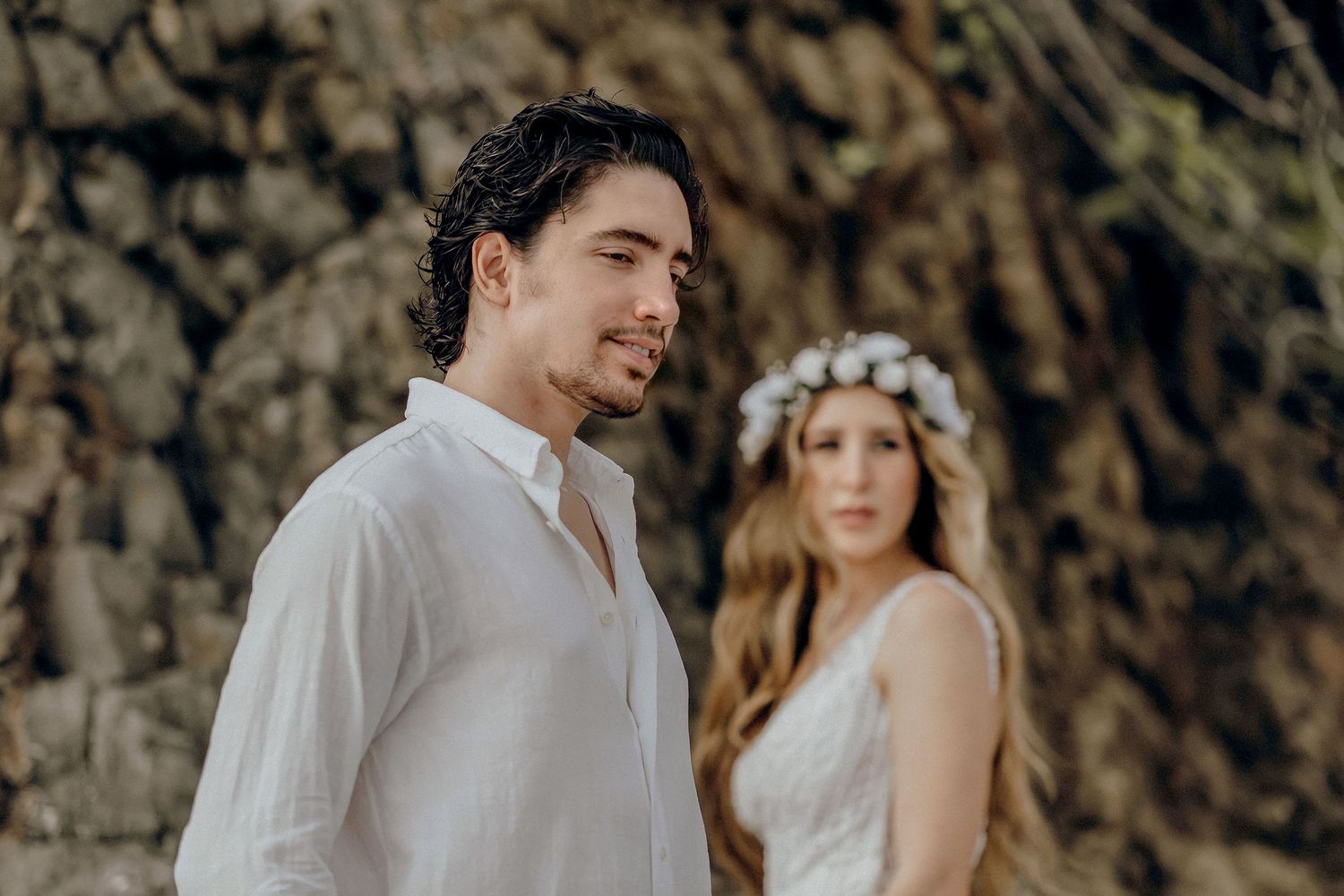 Couple in wedding attire poses together in a rustic outdoor setting.