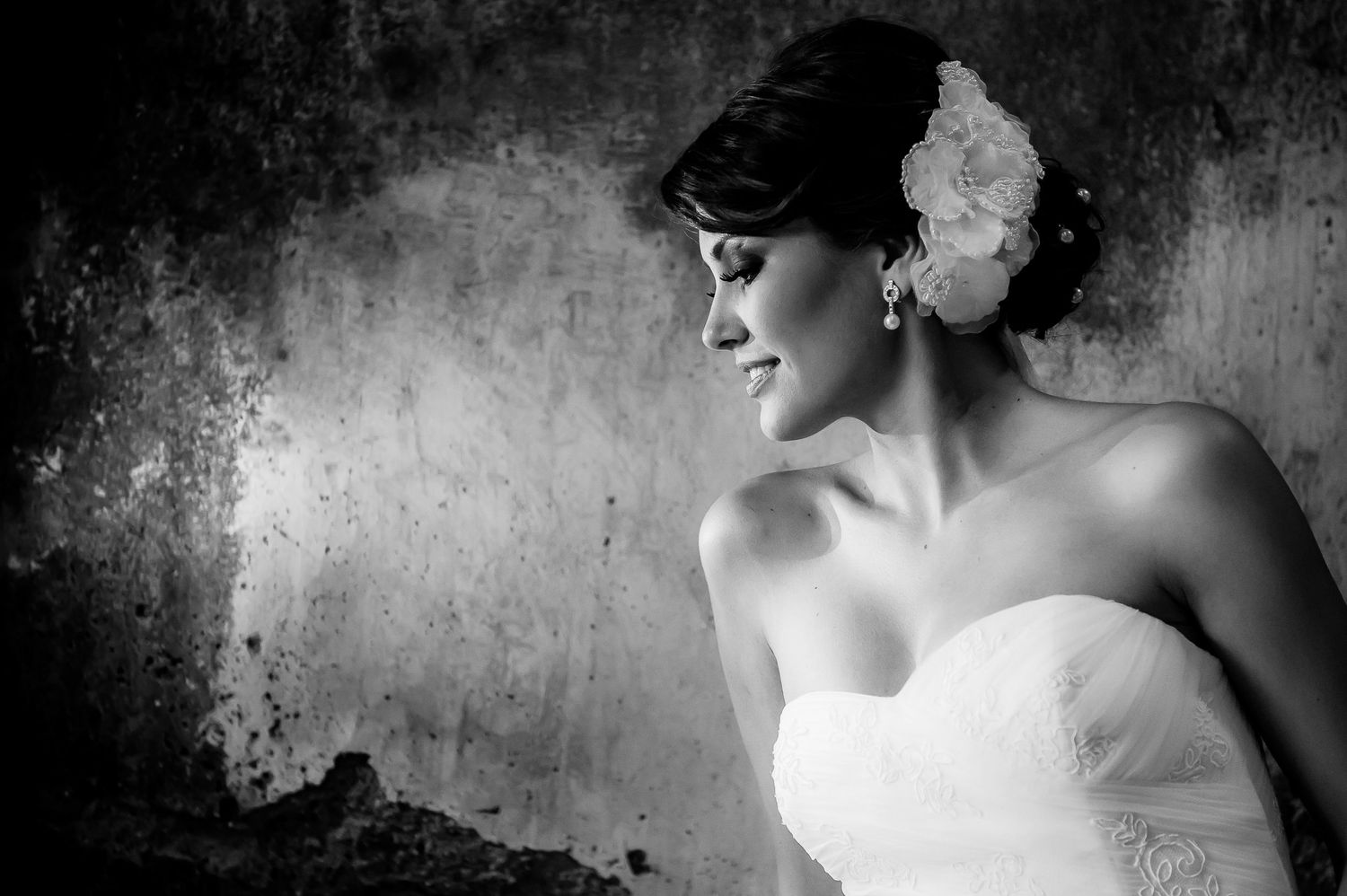 A black and white portrait of a bride wearing a strapless gown and floral hair accessory.