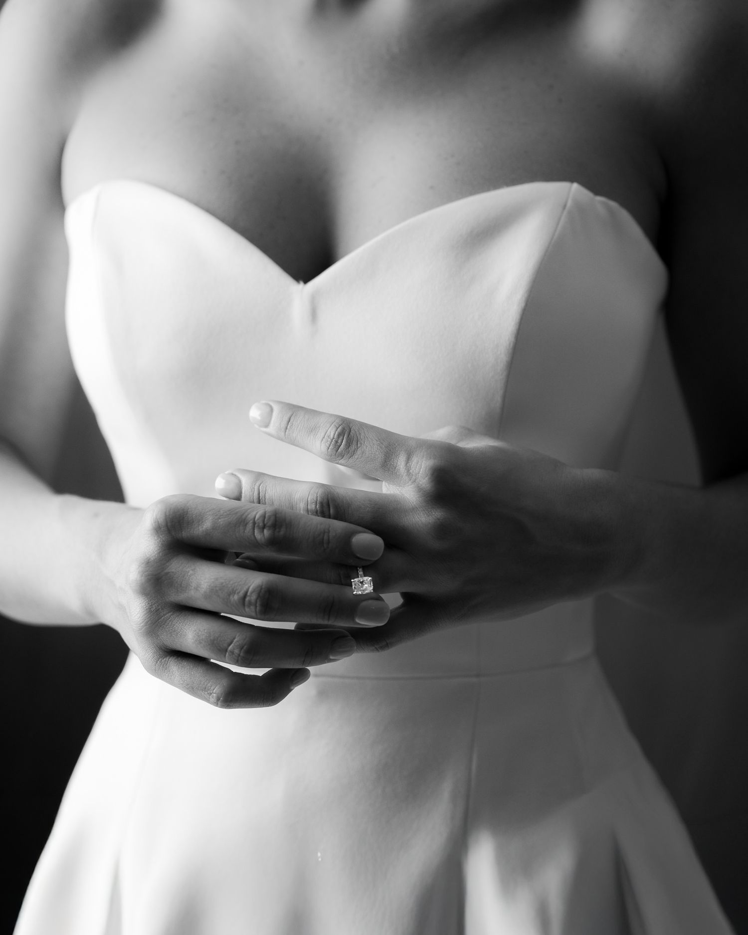 Black and white detail of hands with wedding rings against white dress.