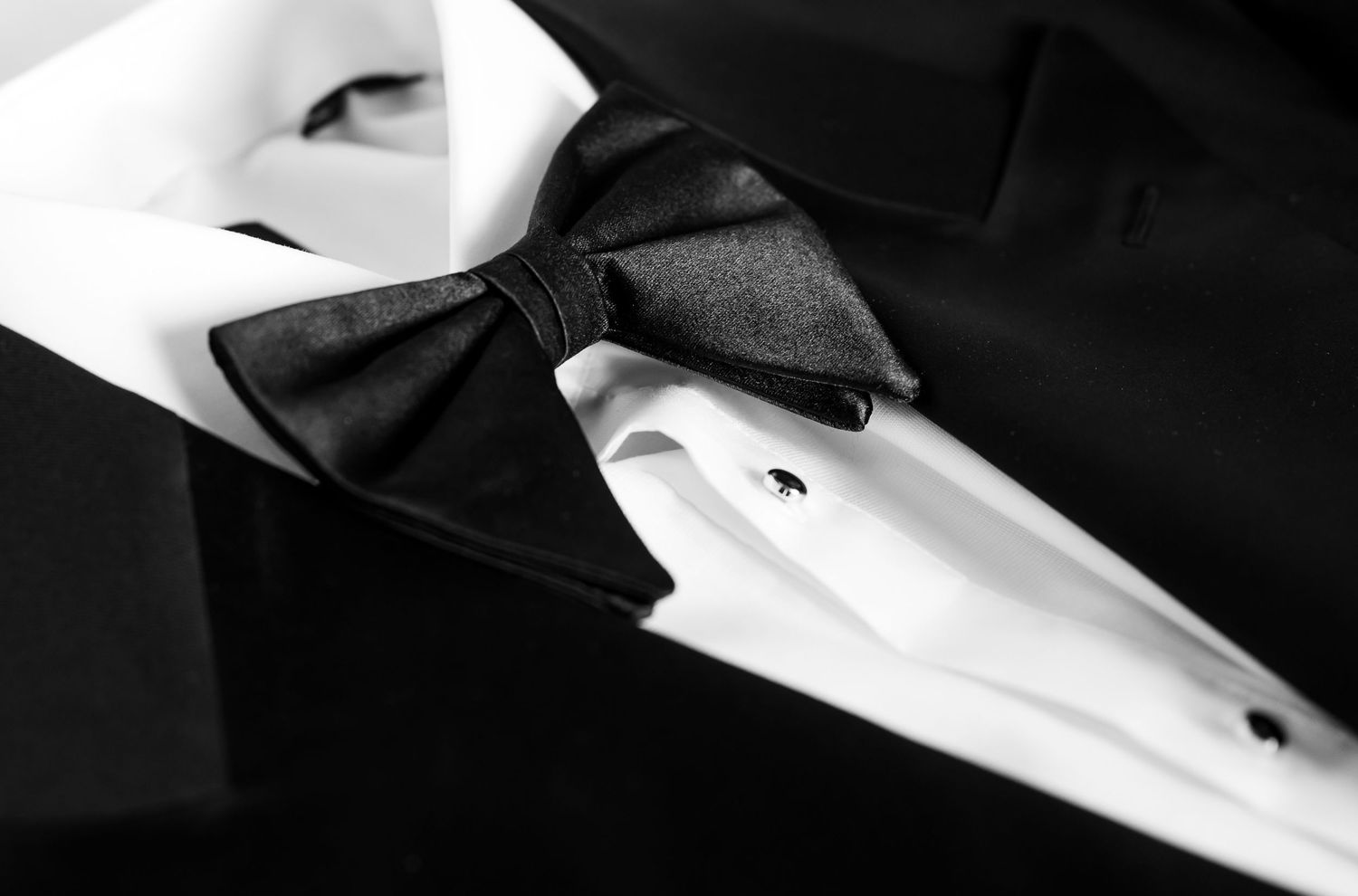 Black and white close-up of a tuxedo with a silk bow tie and white dress shirt with studs.