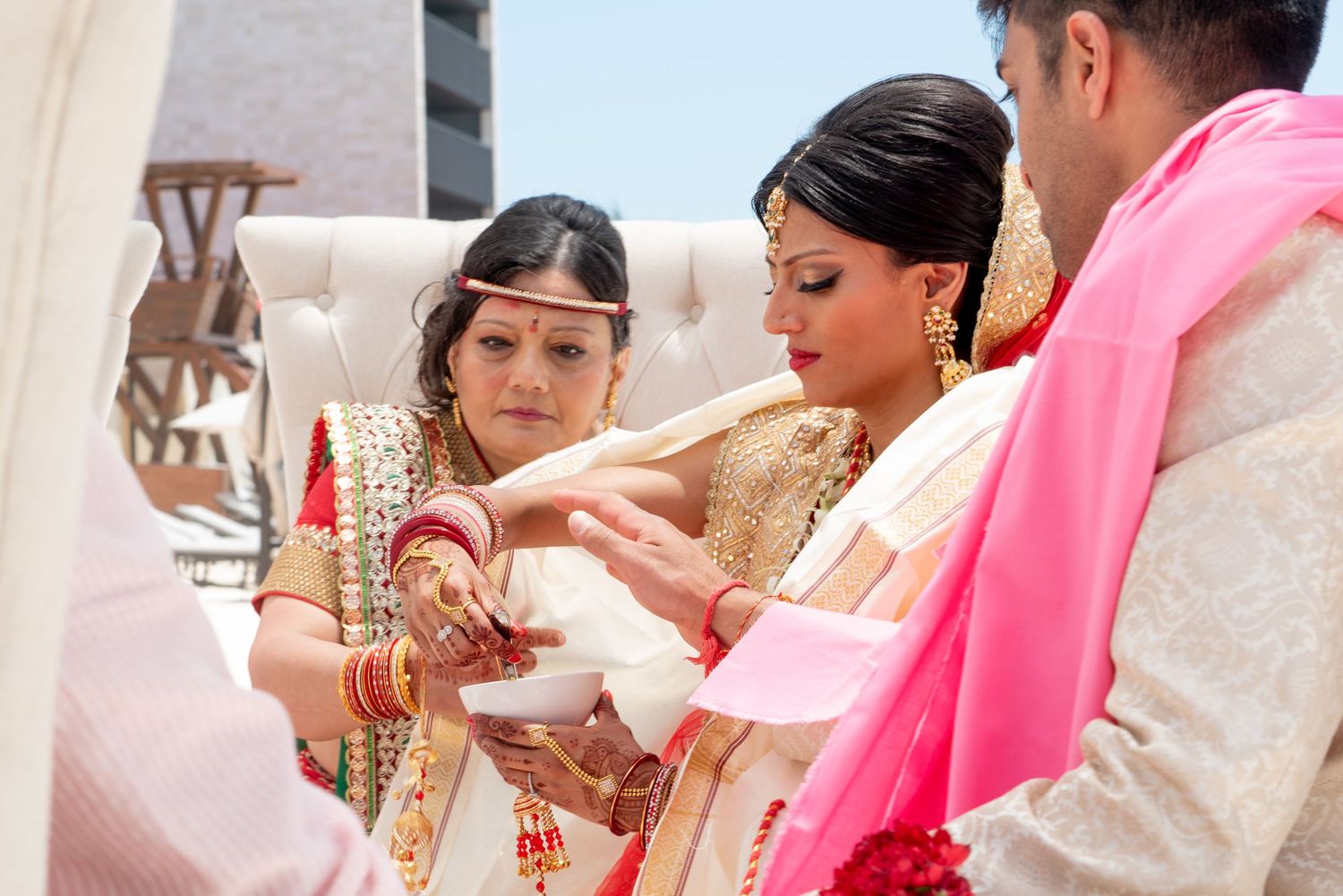 Indian bride in white and gold saree participates in traditional Hindu wedding ceremony with family members.