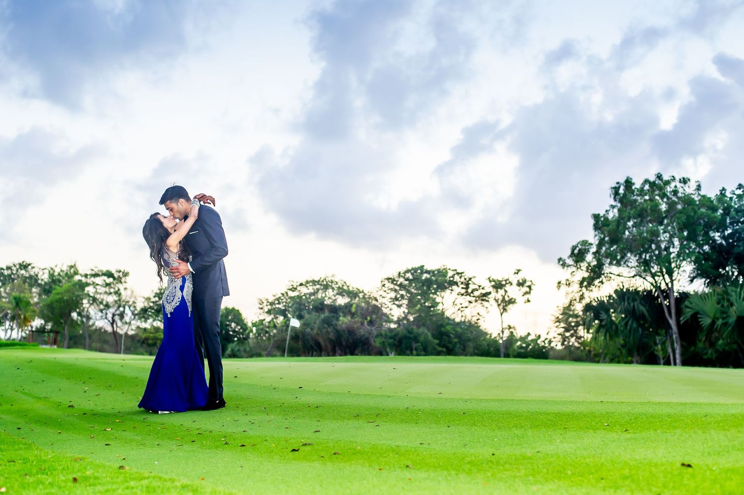 Couple sharing a romantic embrace on a lush green golf course under a dramatic cloudy sky.