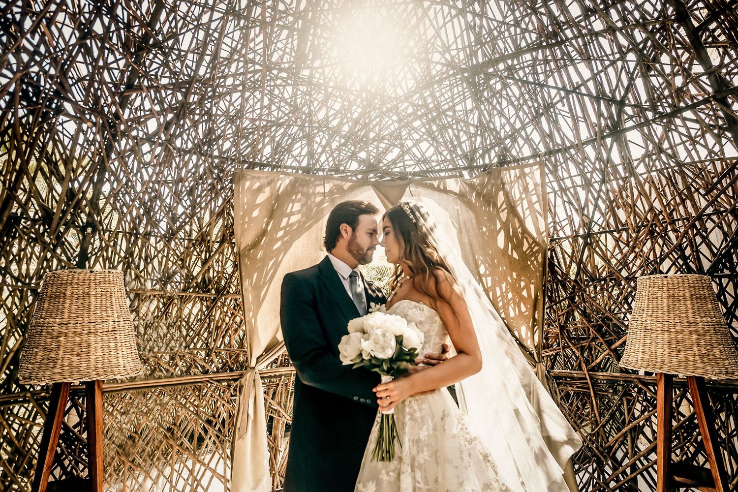 Wedding couple embraces under a natural archway with golden sunlight filtering through.