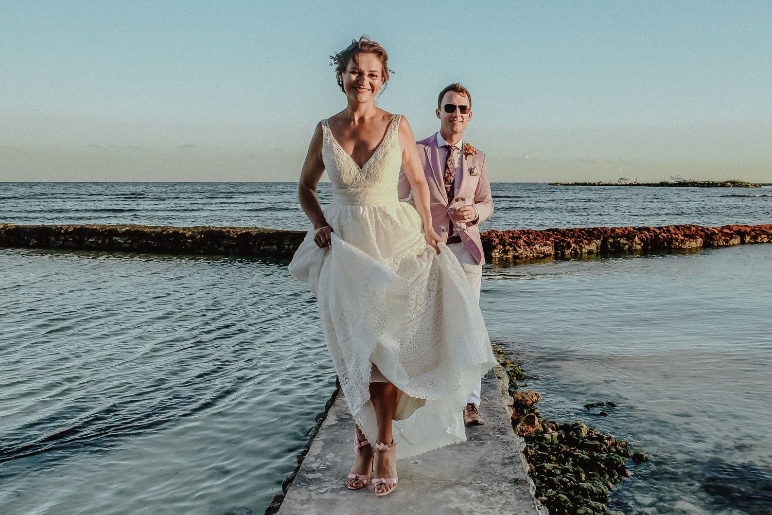 Couple walking along a seaside path during sunset at their beach wedding.