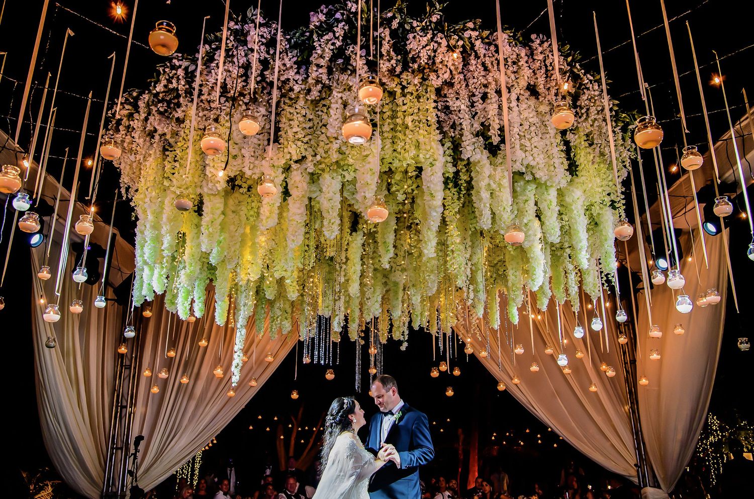 Luxurious wedding venue ceiling adorned with hanging floral arrangements and ambient lighting.